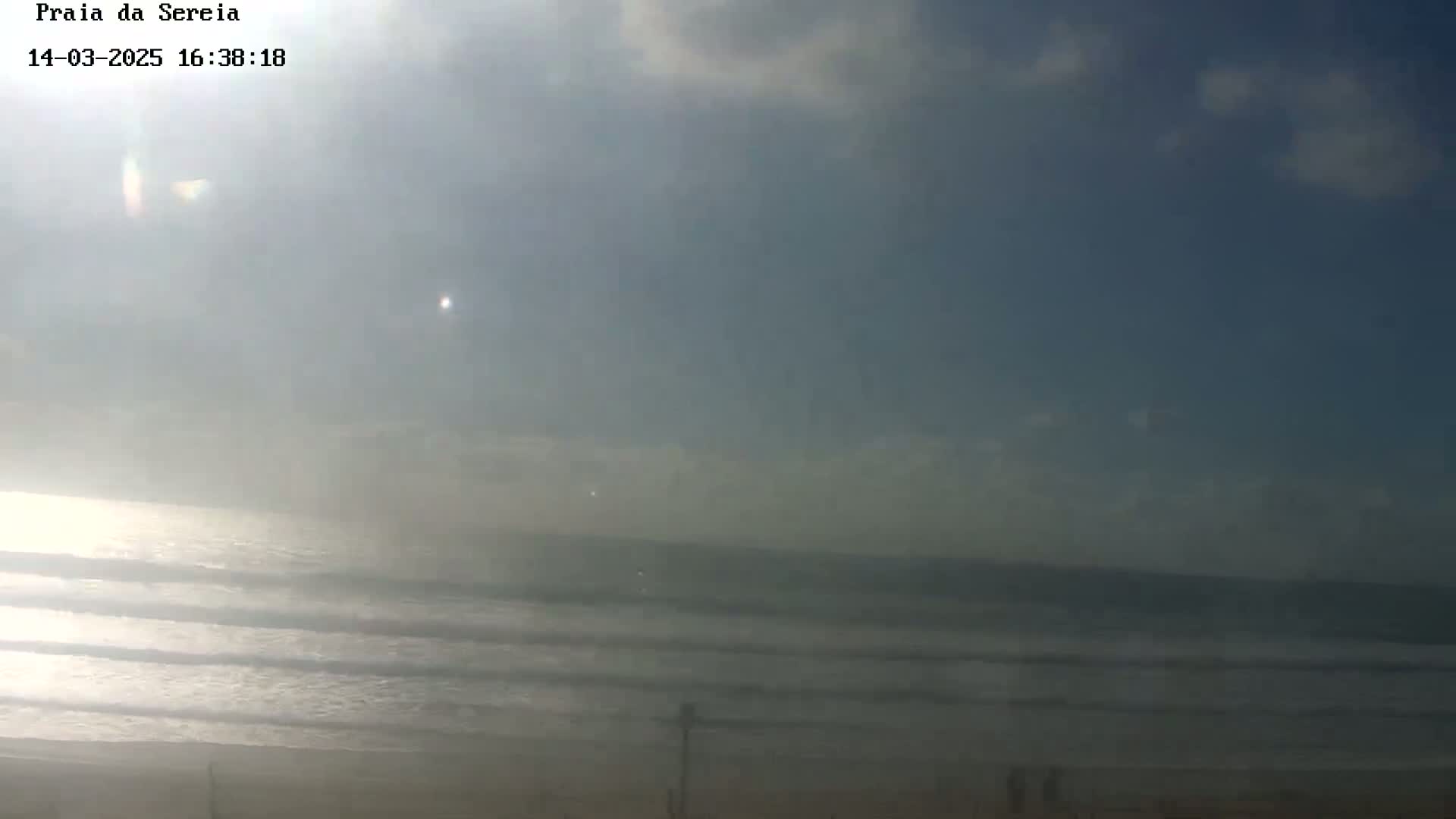 A hazy sunny day at a beach shows gentle waves rolling onto the shore.