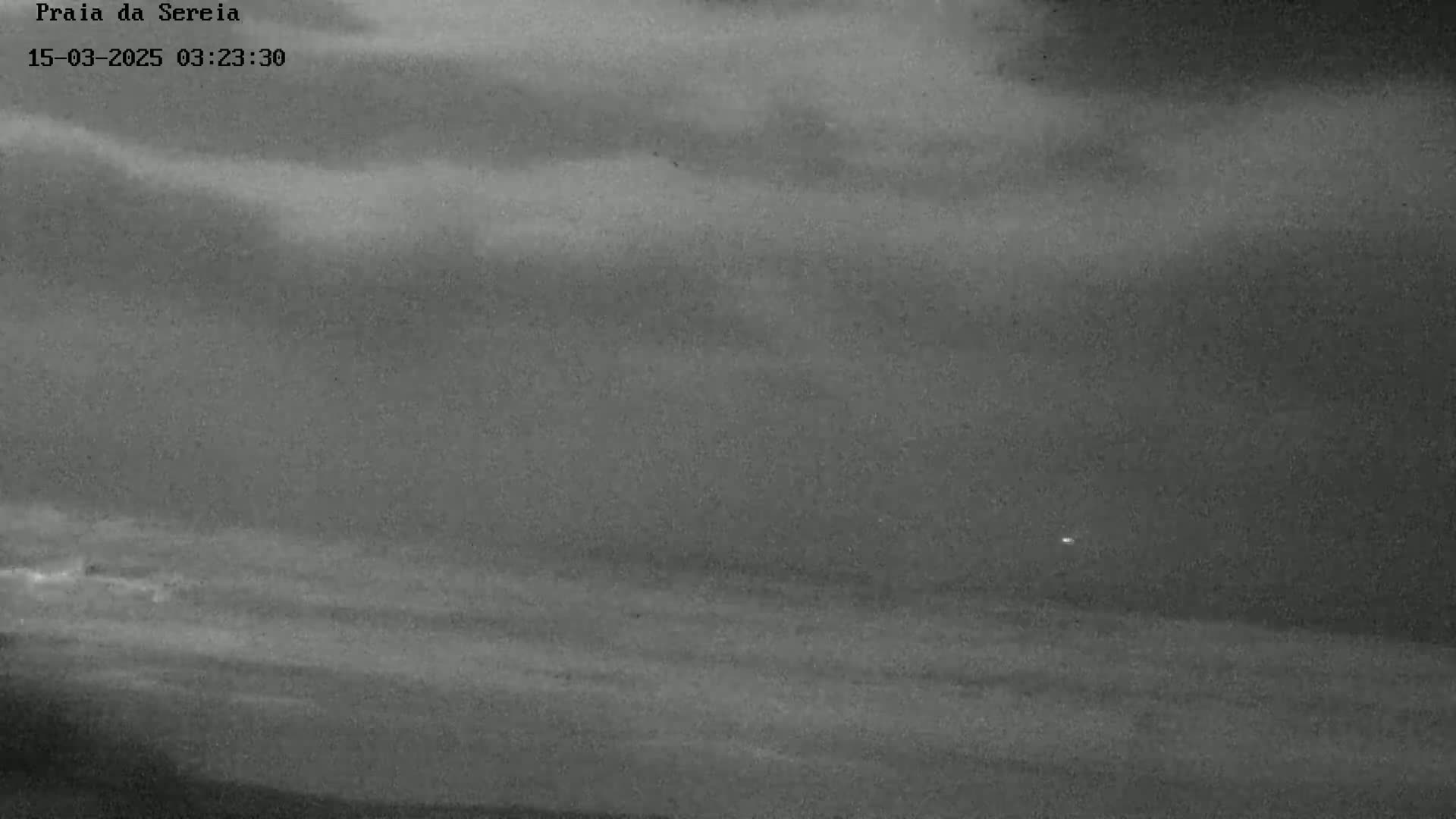 A low-light, nighttime image shows a dark, cloudy sky over a flat, dark expanse of water.