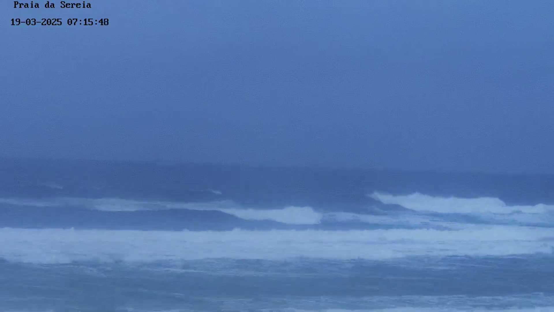A hazy, overcast sky looms over a turbulent ocean with waves breaking in the distance.