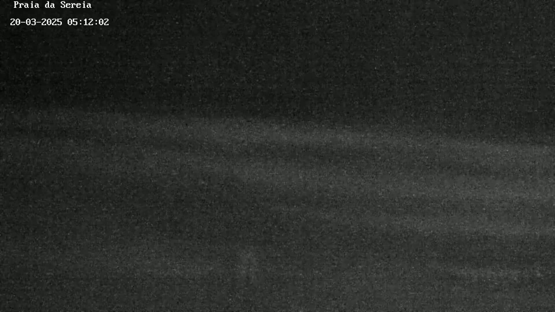 A dark, grainy image shows a mostly uniform dark gray surface with subtle horizontal variations in shading.