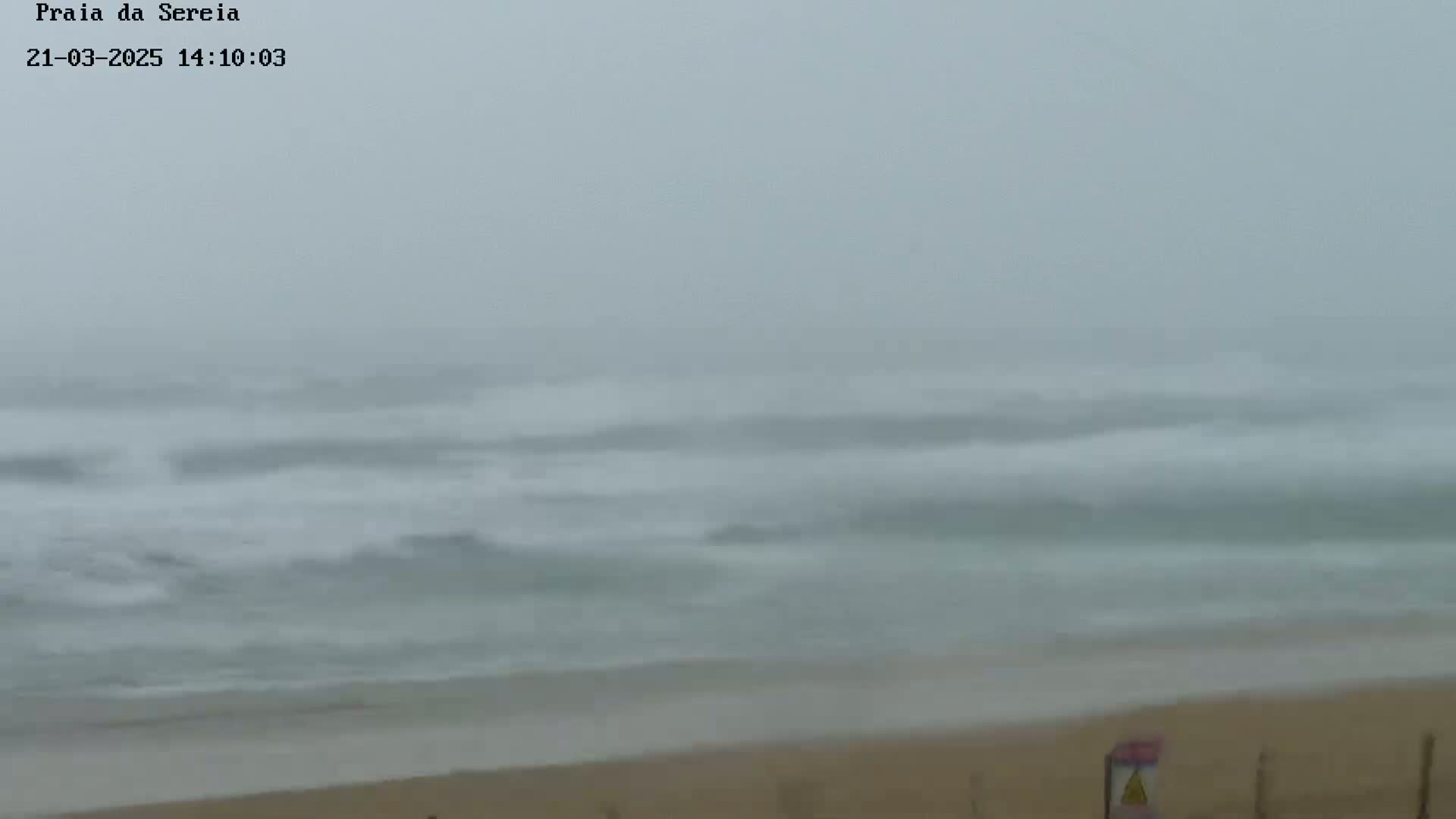 A sandy beach is visible under a foggy sky with choppy waves rolling onto the shore.