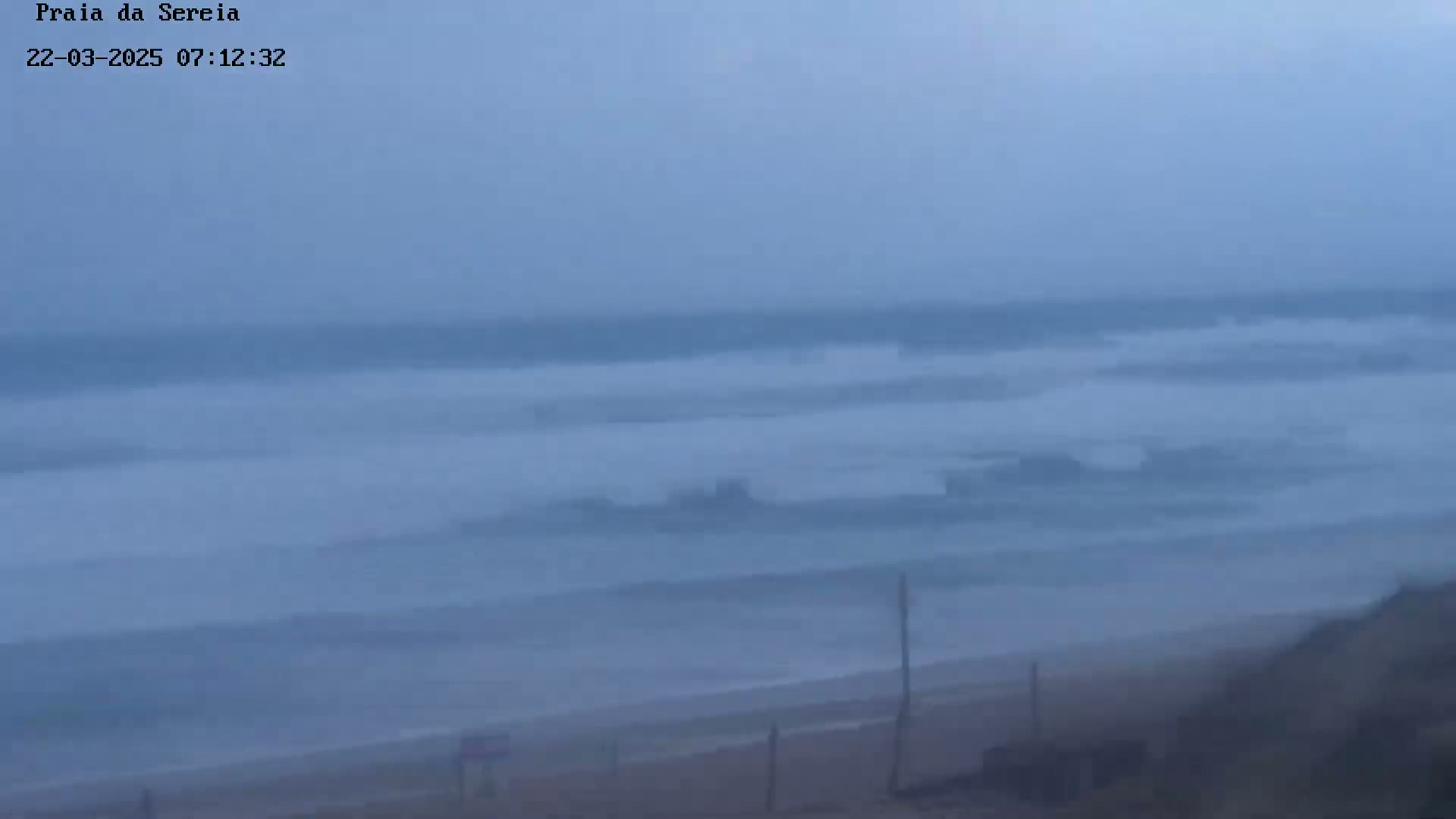 A hazy, overcast day shows a beach with a distant, choppy ocean.