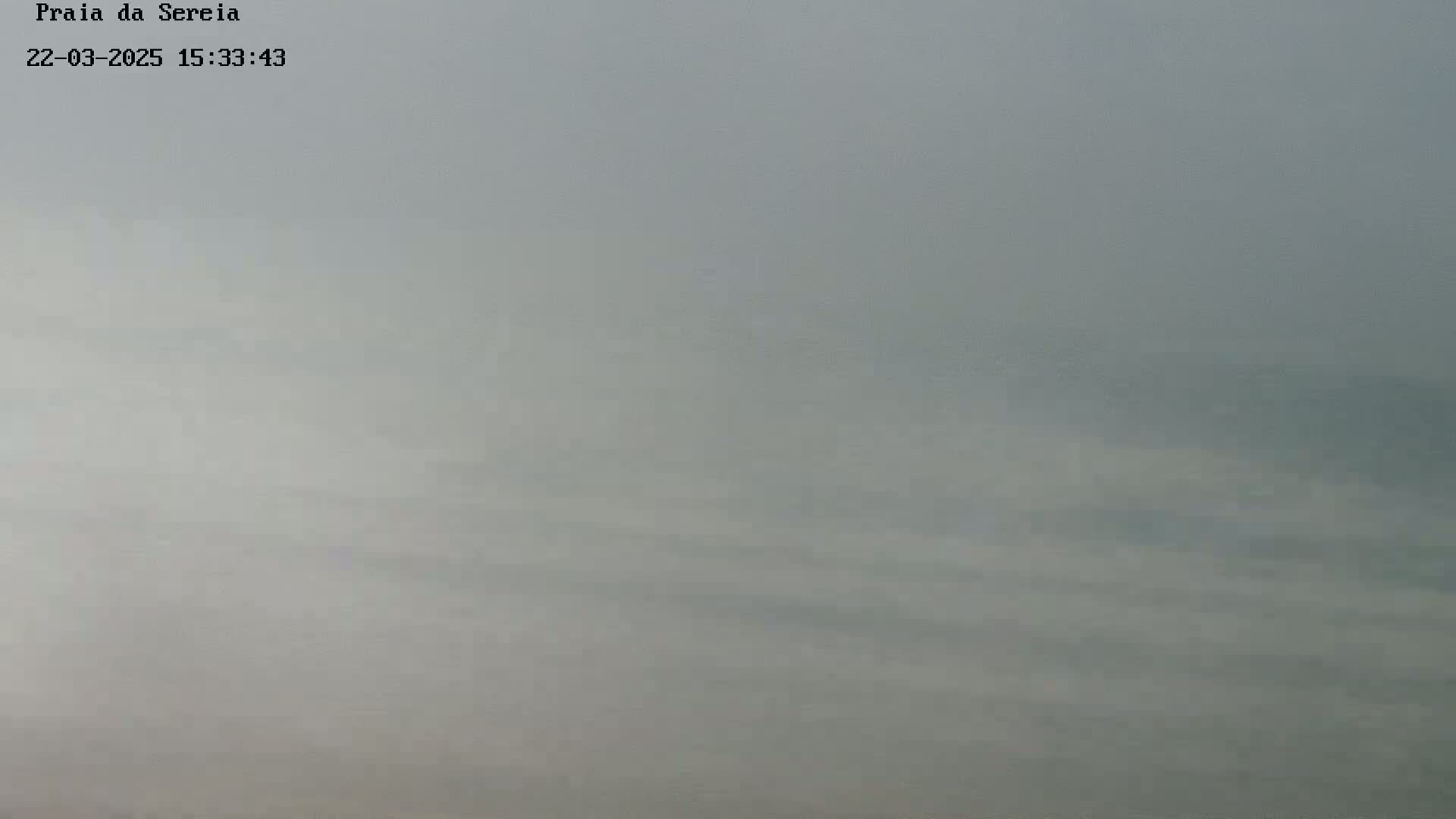 A foggy or hazy view of a body of water, possibly the ocean, is visible under a cloudy sky.