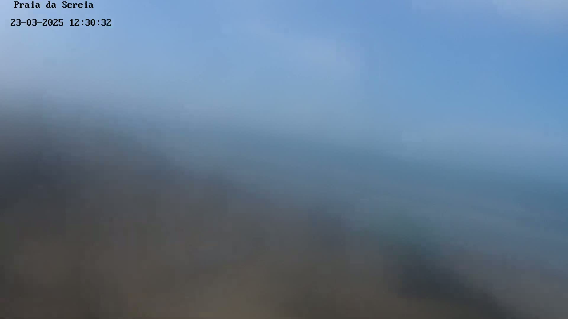 A hazy, out-of-focus view of a body of water under a clear, light blue sky.