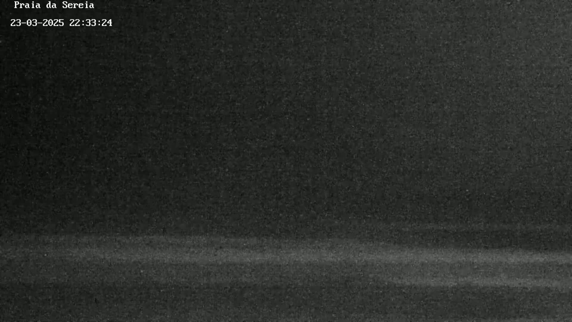 A grainy, dark image shows a mostly black, horizontal expanse, possibly a nighttime beach or similar landscape under a dark sky.