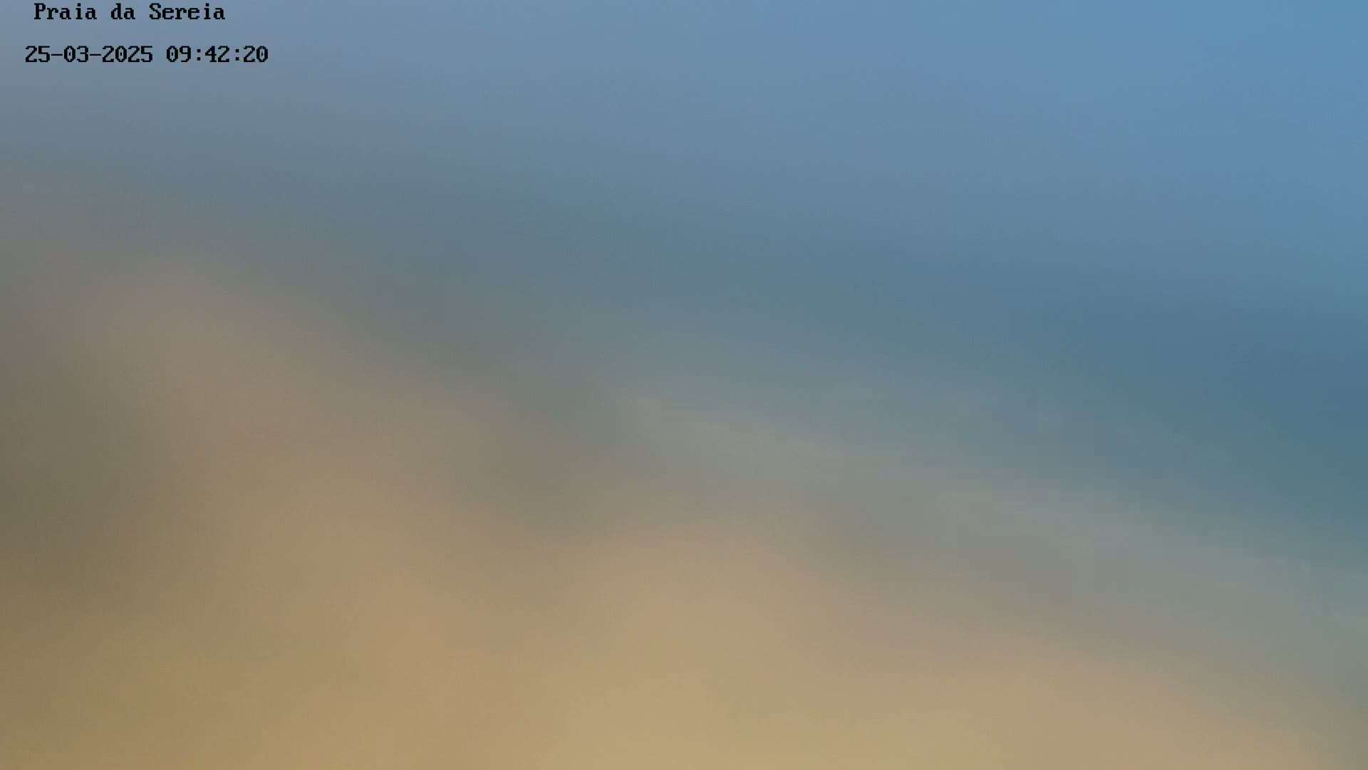 A blurry image shows a hazy, light-blue sky above a muted beige and brown landscape.