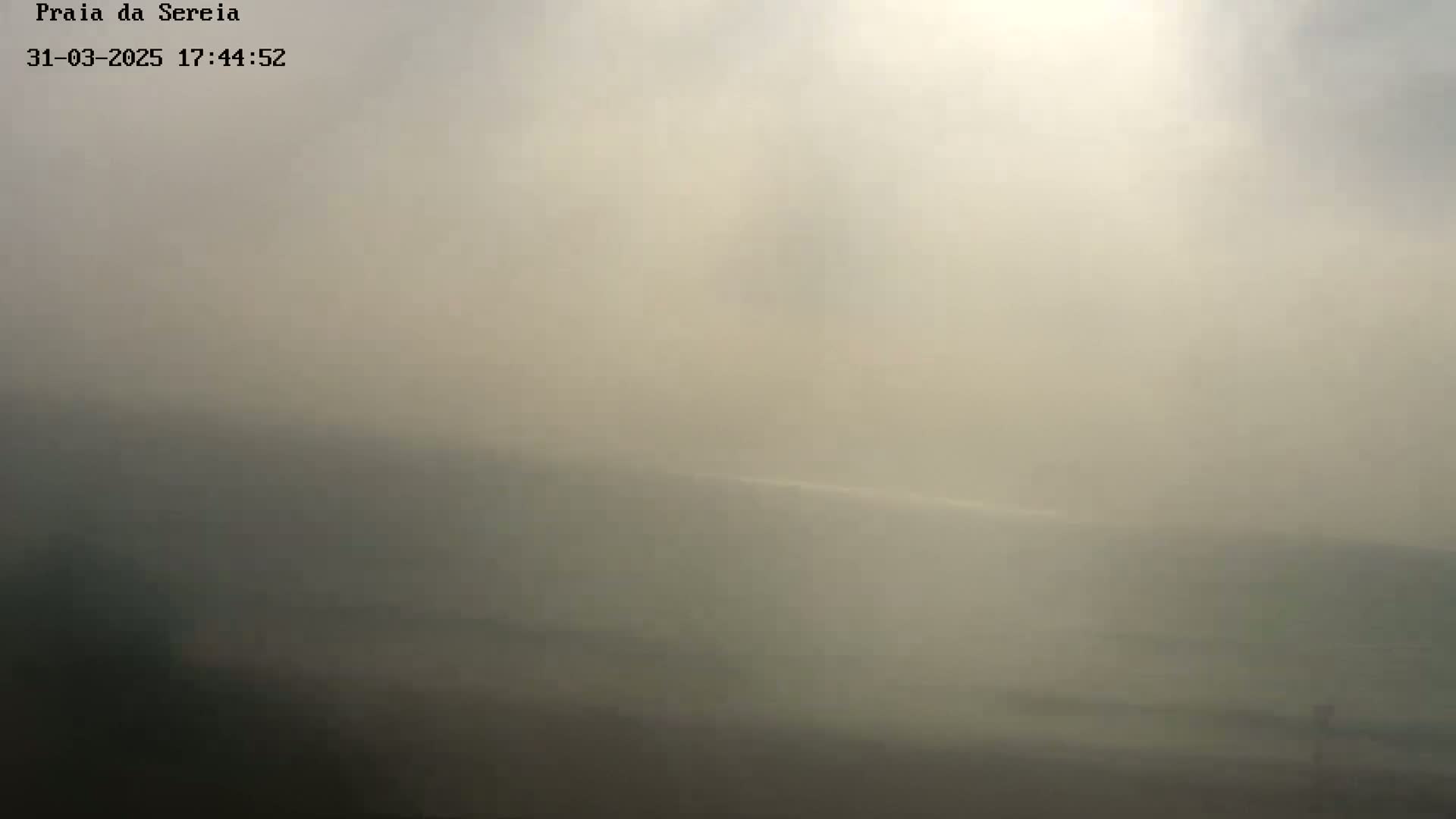 A hazy, indistinct view of a landscape, possibly coastal, under a heavily overcast sky.