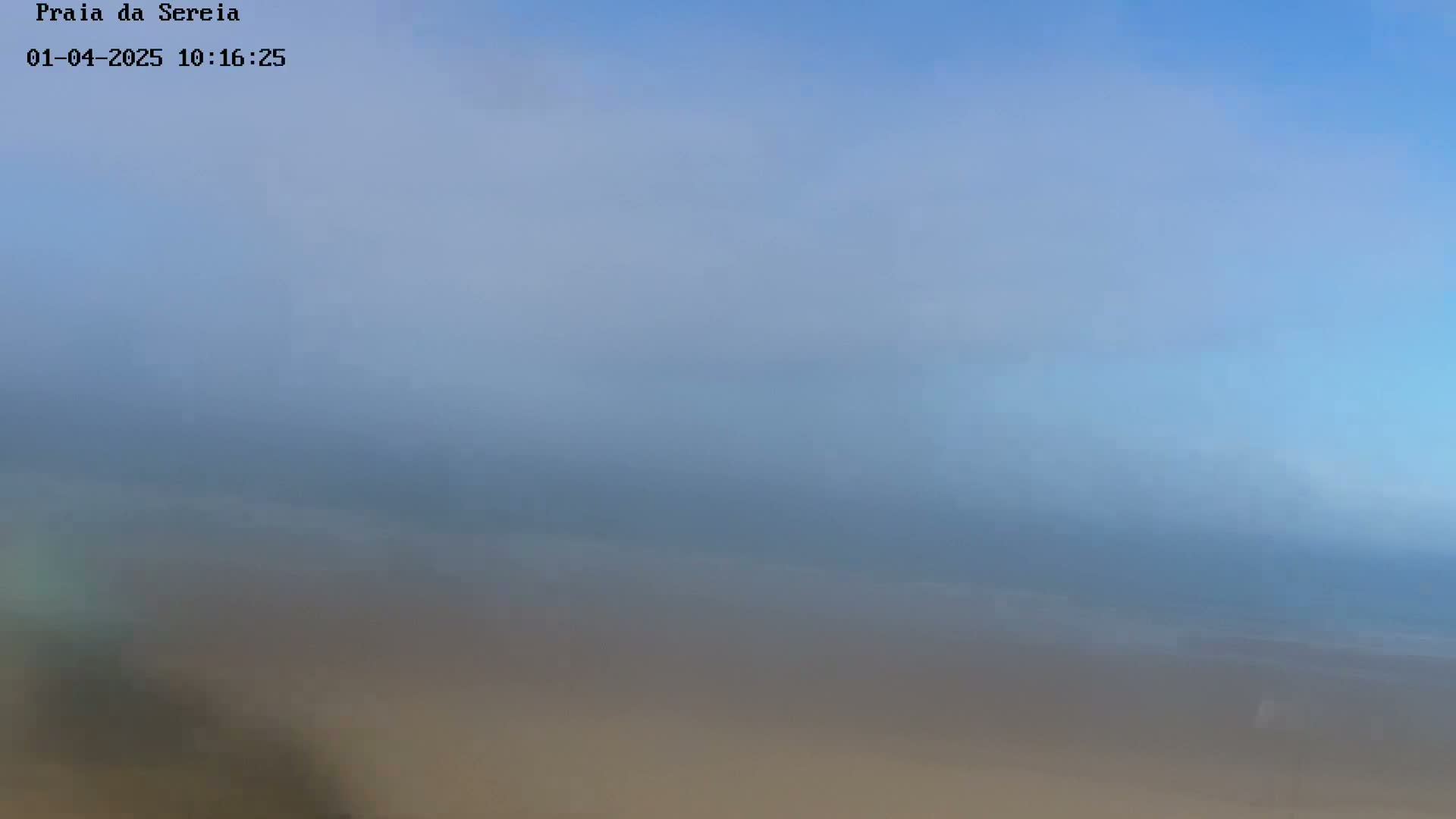 A hazy, blurry image shows a beach scene under a mostly clear, light-blue sky.
