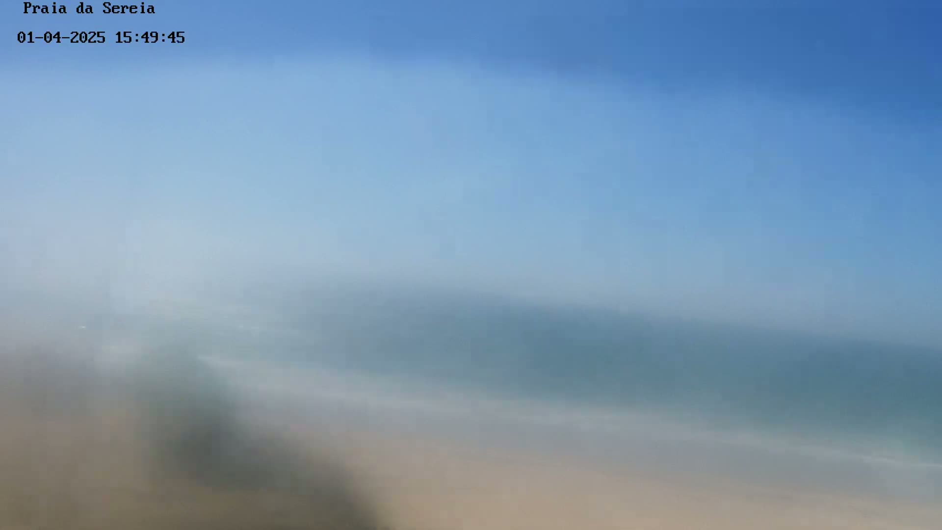 A hazy, blurry image shows a beach and ocean under a clear blue sky.