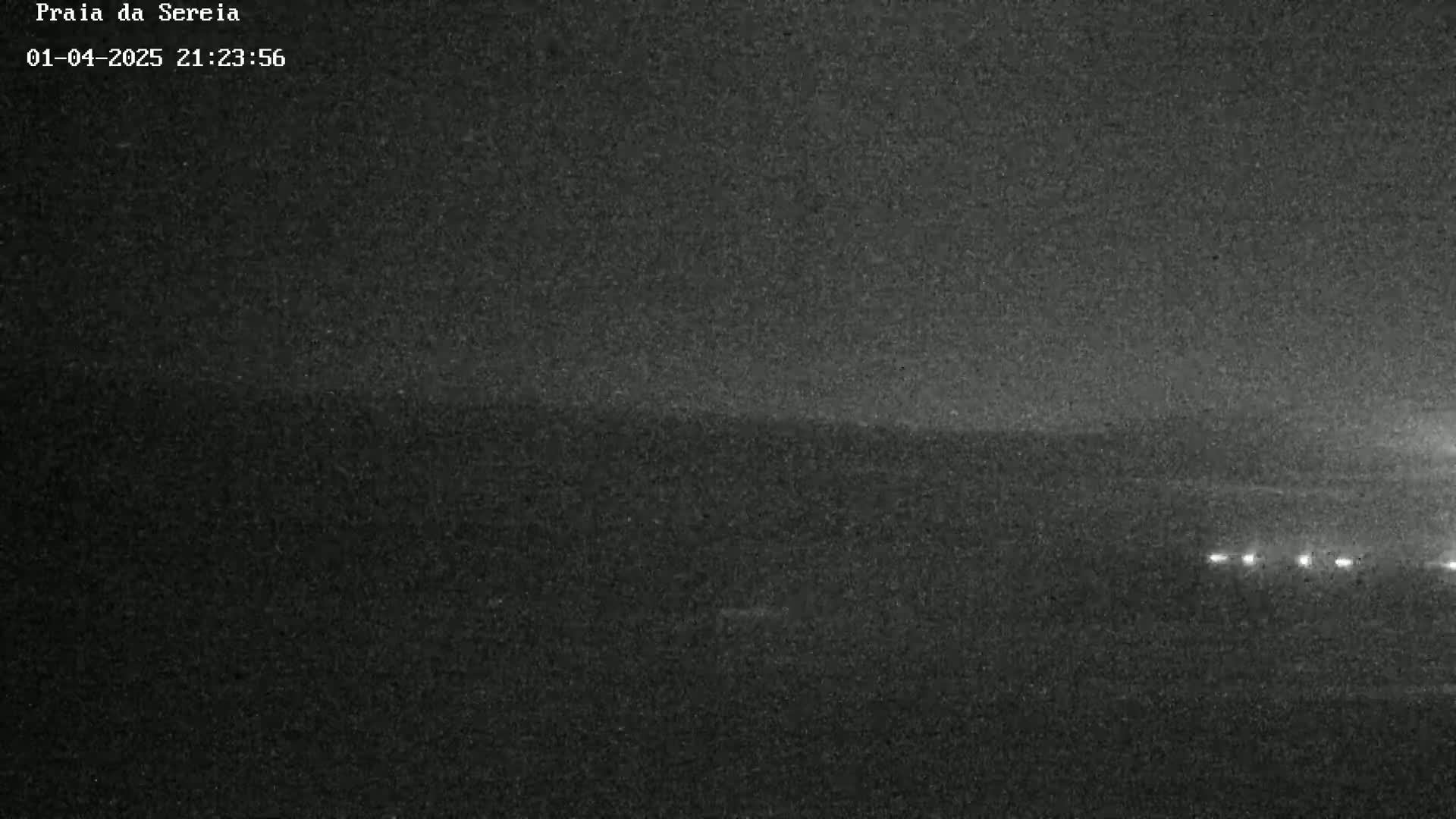 A dark, nighttime view of a landscape with a few distant lights visible.