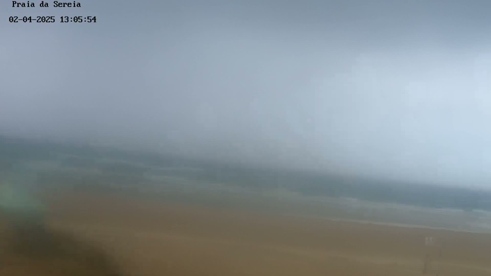 A hazy, overcast view shows a beach with a muted-colored ocean in the distance.