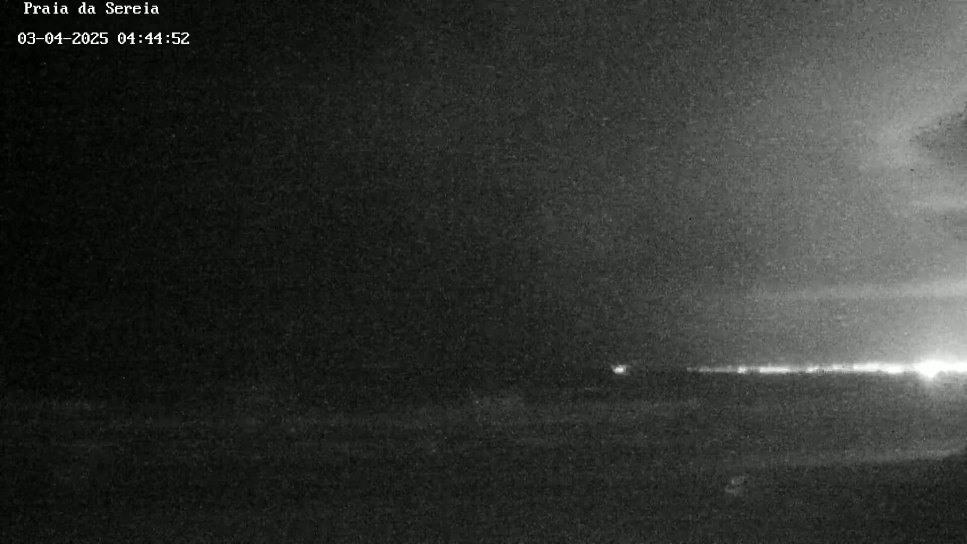 A dark, nighttime scene shows a distant line of lights on the horizon under a mostly clear sky.