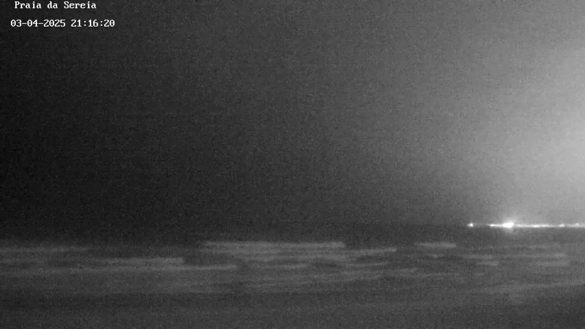 A dark, nighttime beach scene shows a calm ocean under a mostly clear sky.