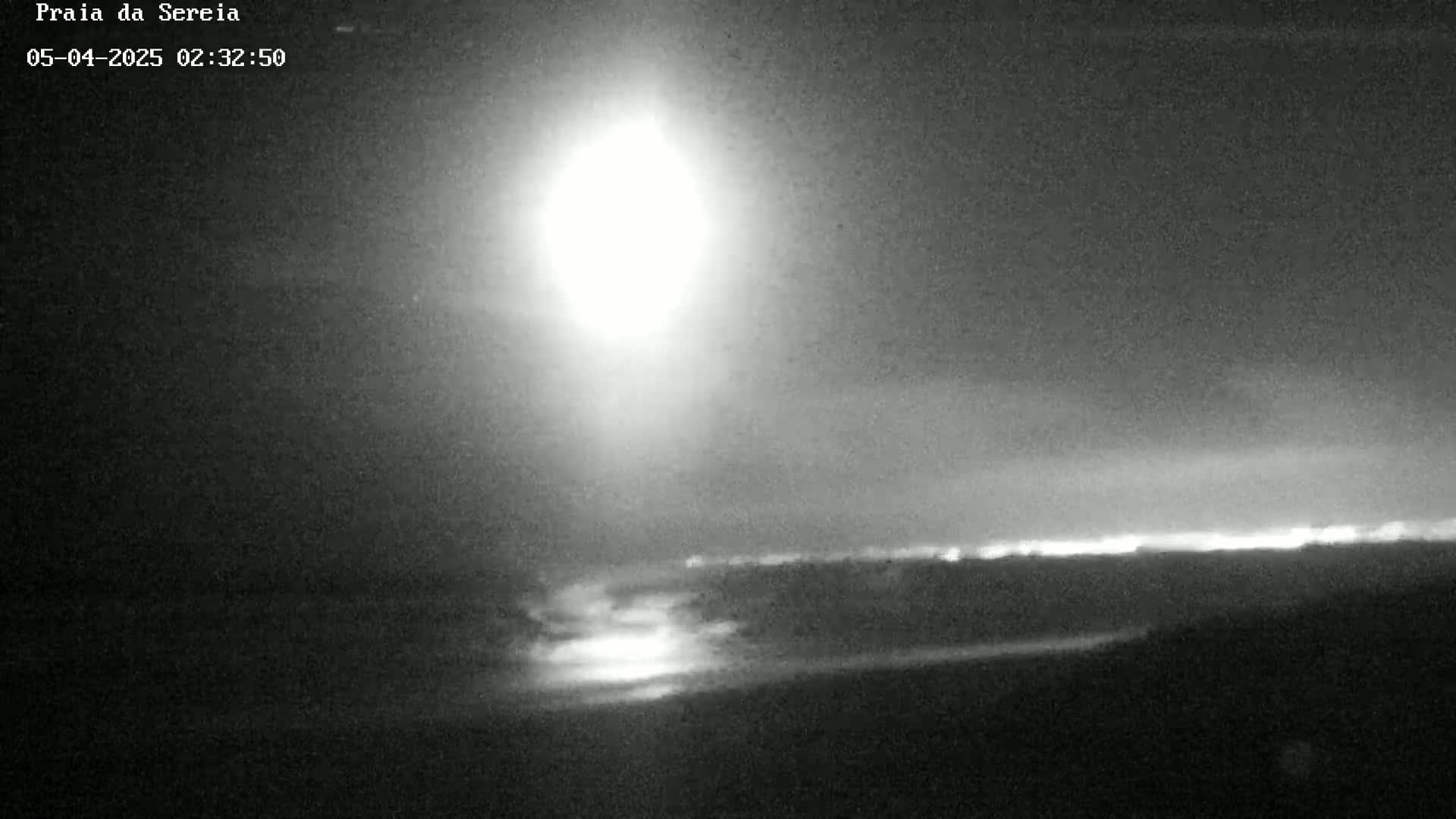 A bright light, possibly the moon, illuminates a dark, nighttime landscape with a distant horizon line.