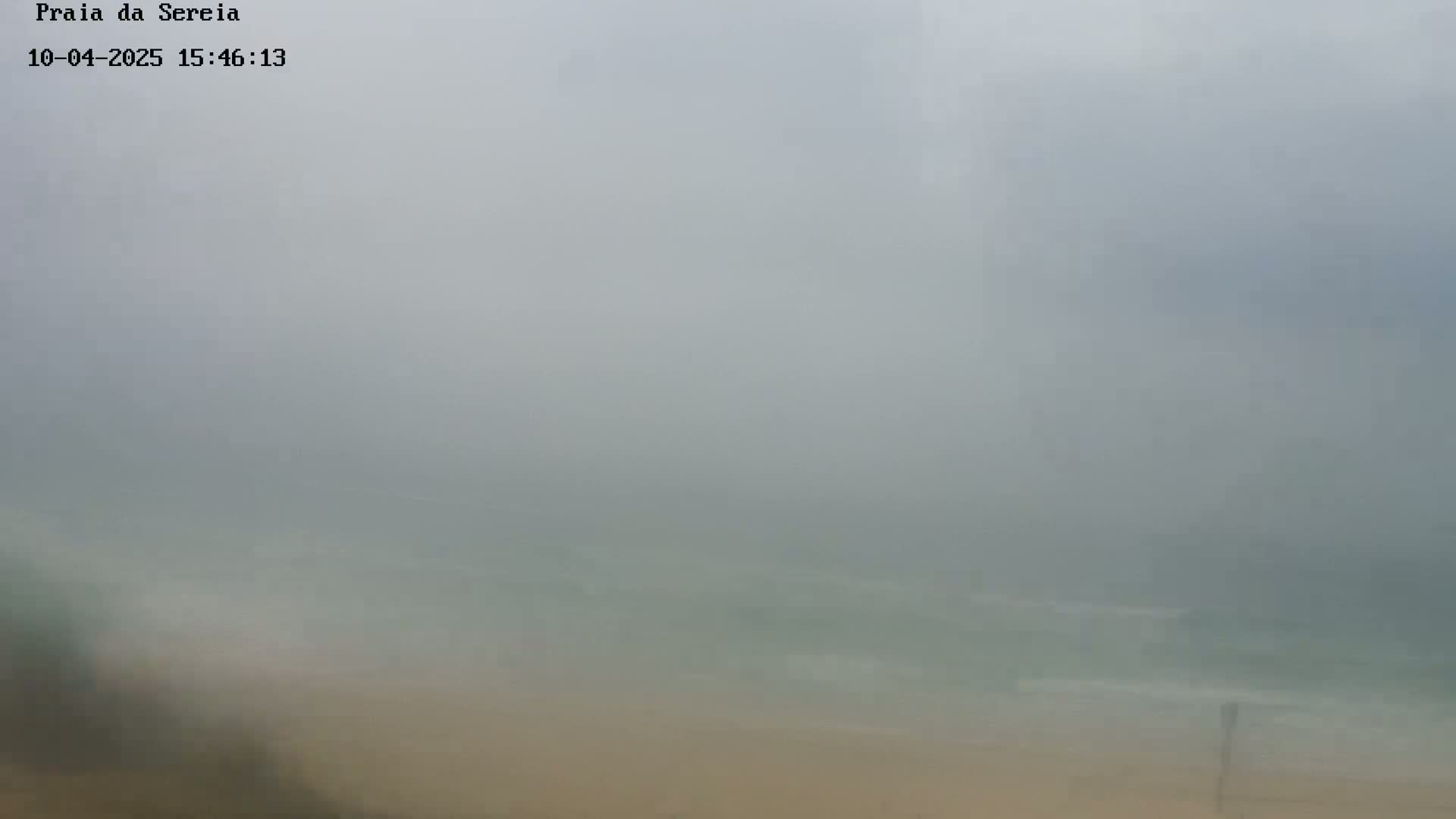 A foggy beach scene shows a hazy view of the ocean and sandy shore.