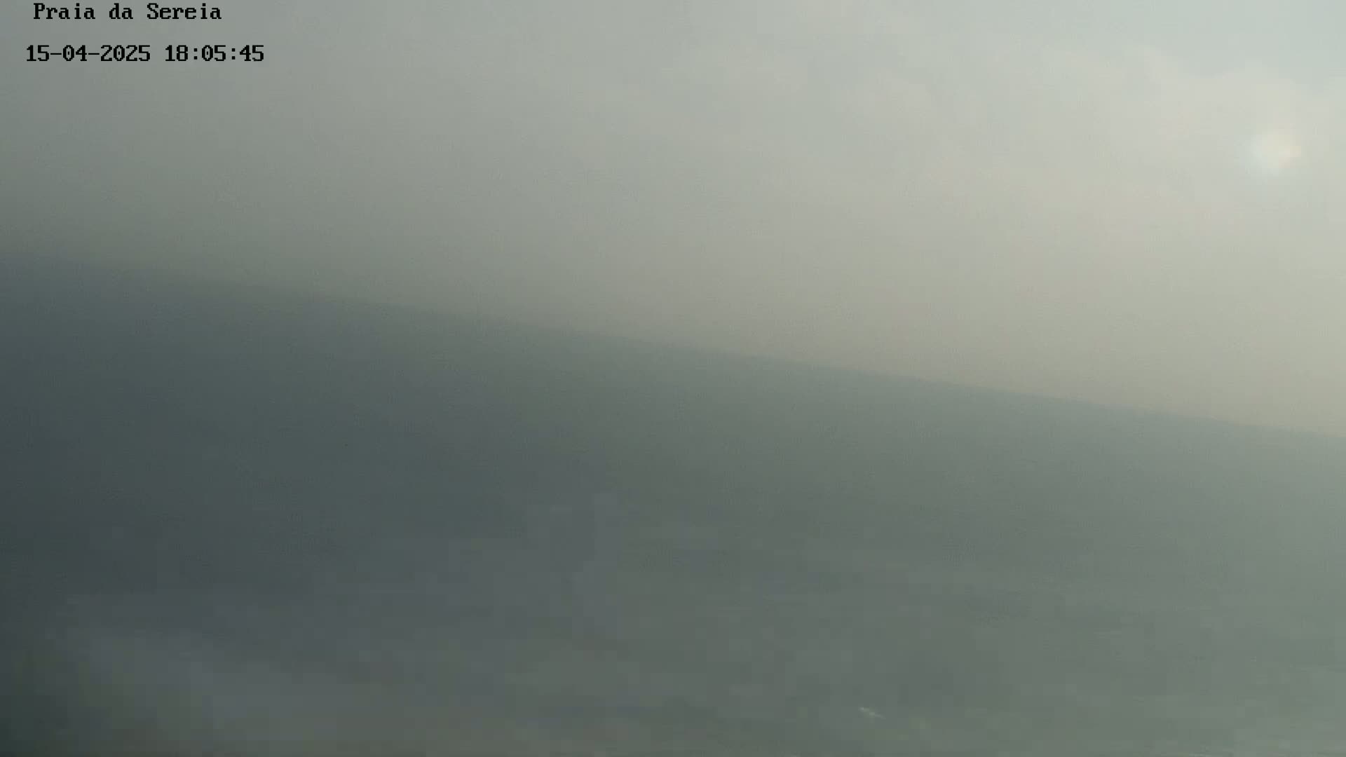 A hazy, overcast sky obscures a distant, indistinct shoreline.