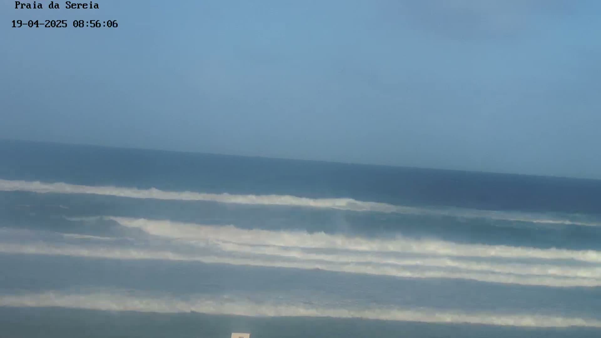 Under a clear sky, several lines of waves break on a dark-blue ocean.