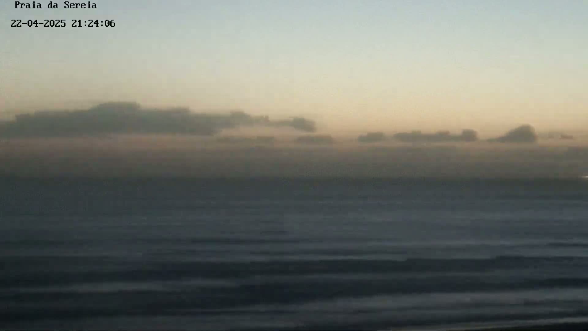 A hazy, calm ocean is visible under a low-lying cloud cover at dusk.