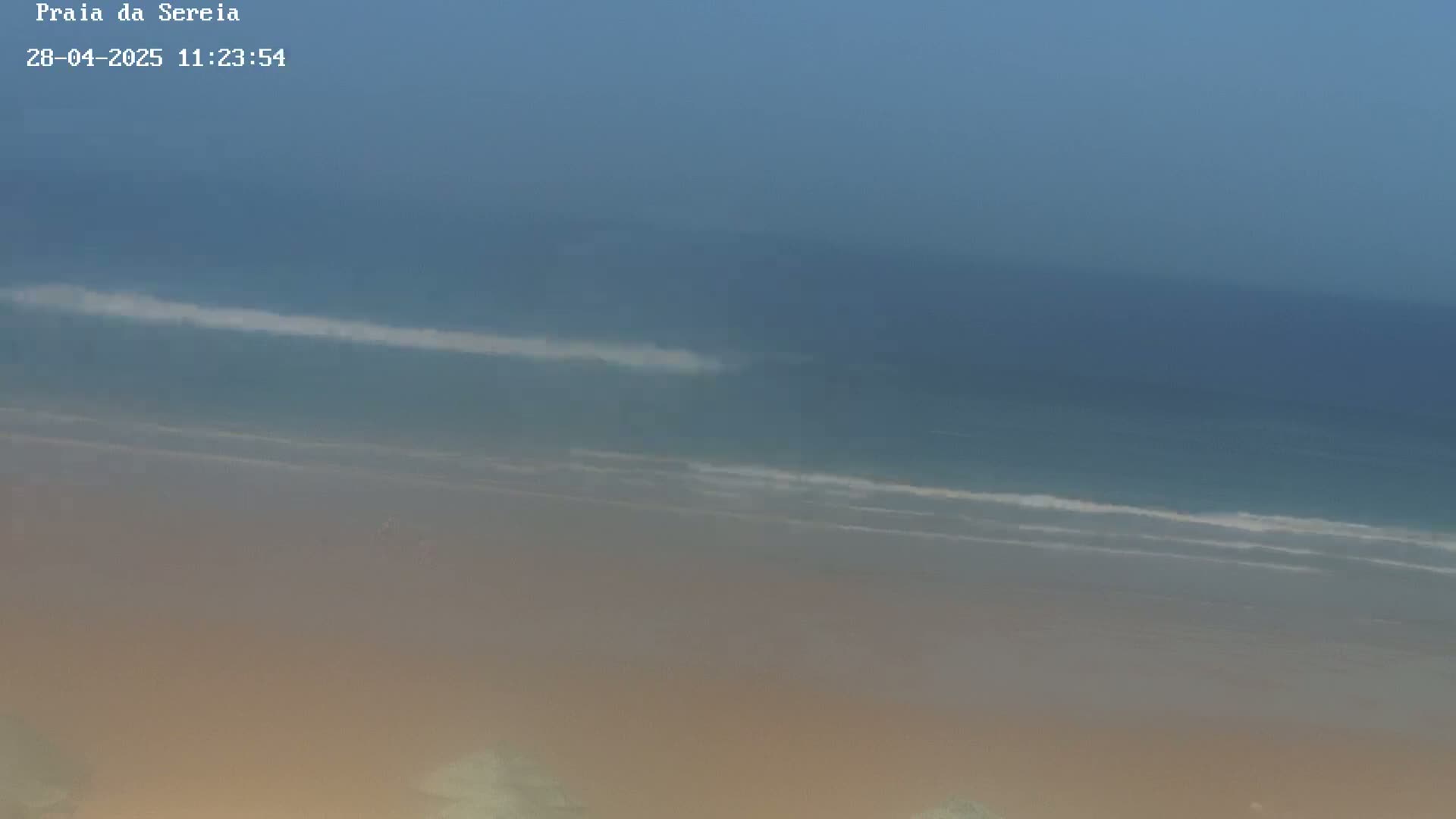 A hazy, overcast day reveals a long, sandy beach with gentle waves lapping the shore.