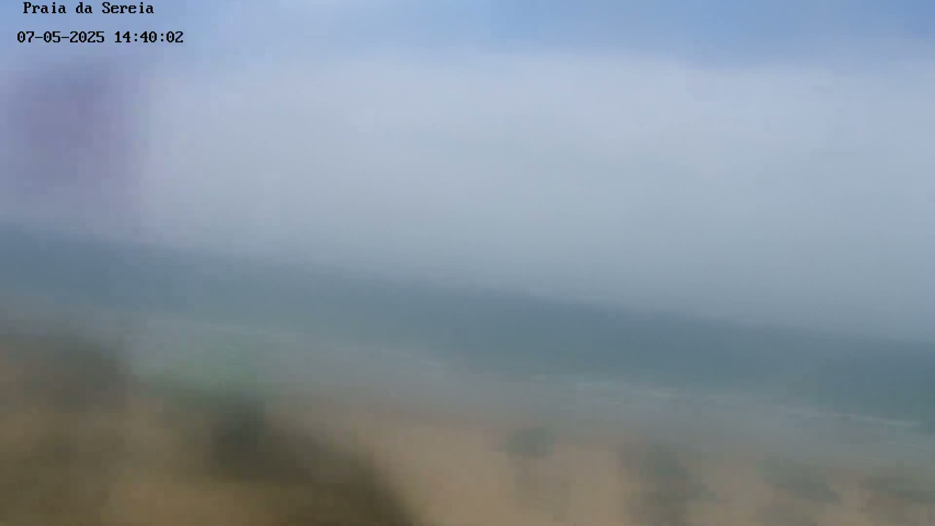 A hazy, blurry view of a beach and ocean under a light blue sky.