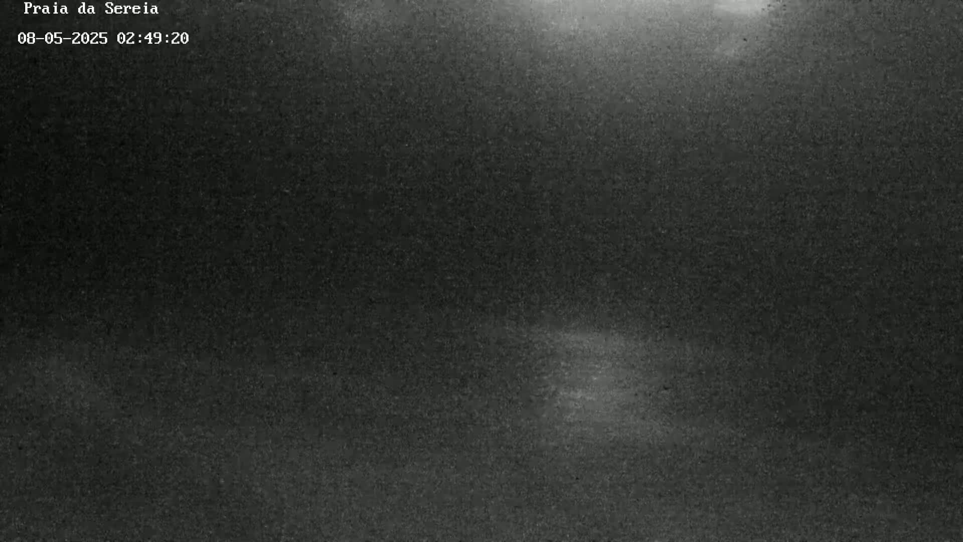 A grainy, dark nighttime image shows a mostly clear sky with a faint, brighter area near the bottom.