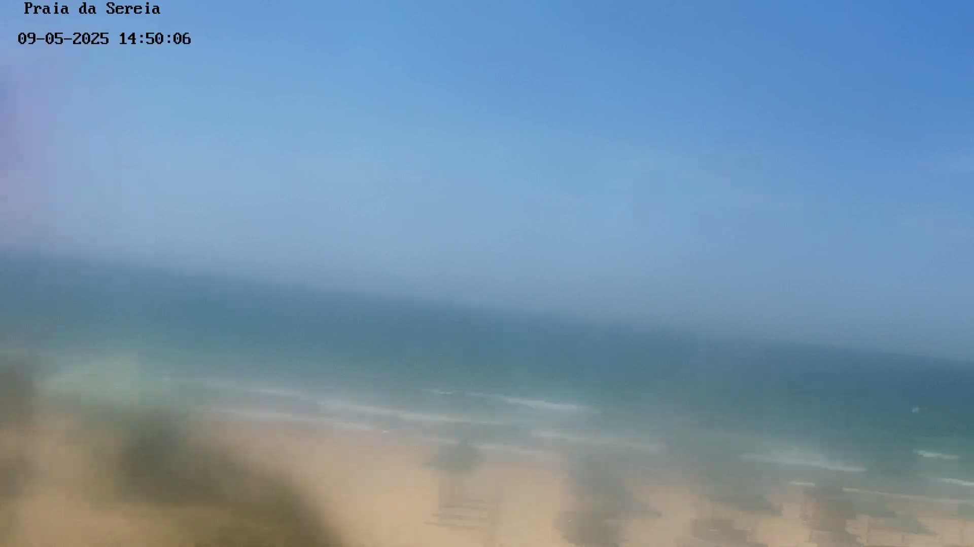 A hazy, sunny day overlooks a calm ocean meeting a sandy beach.