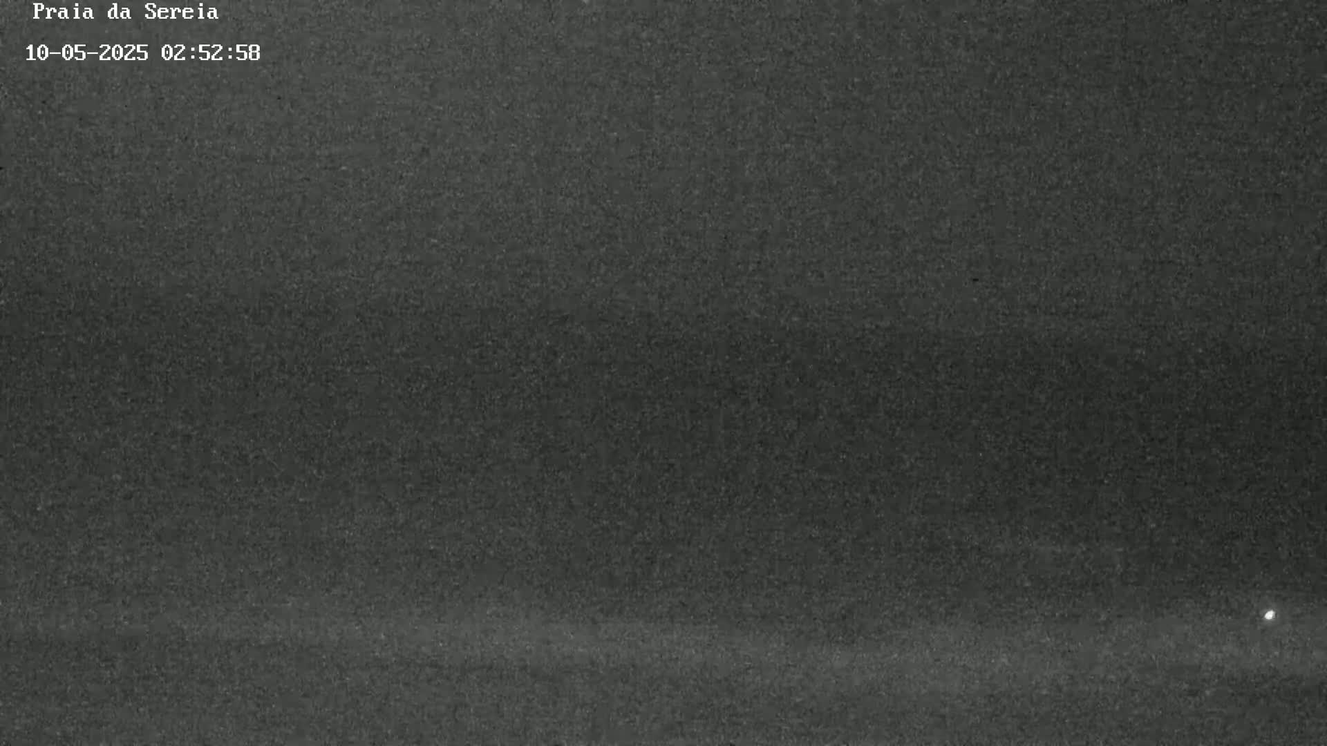 A dark, grainy image shows a nighttime beach scene with a single, small light visible in the far right corner.