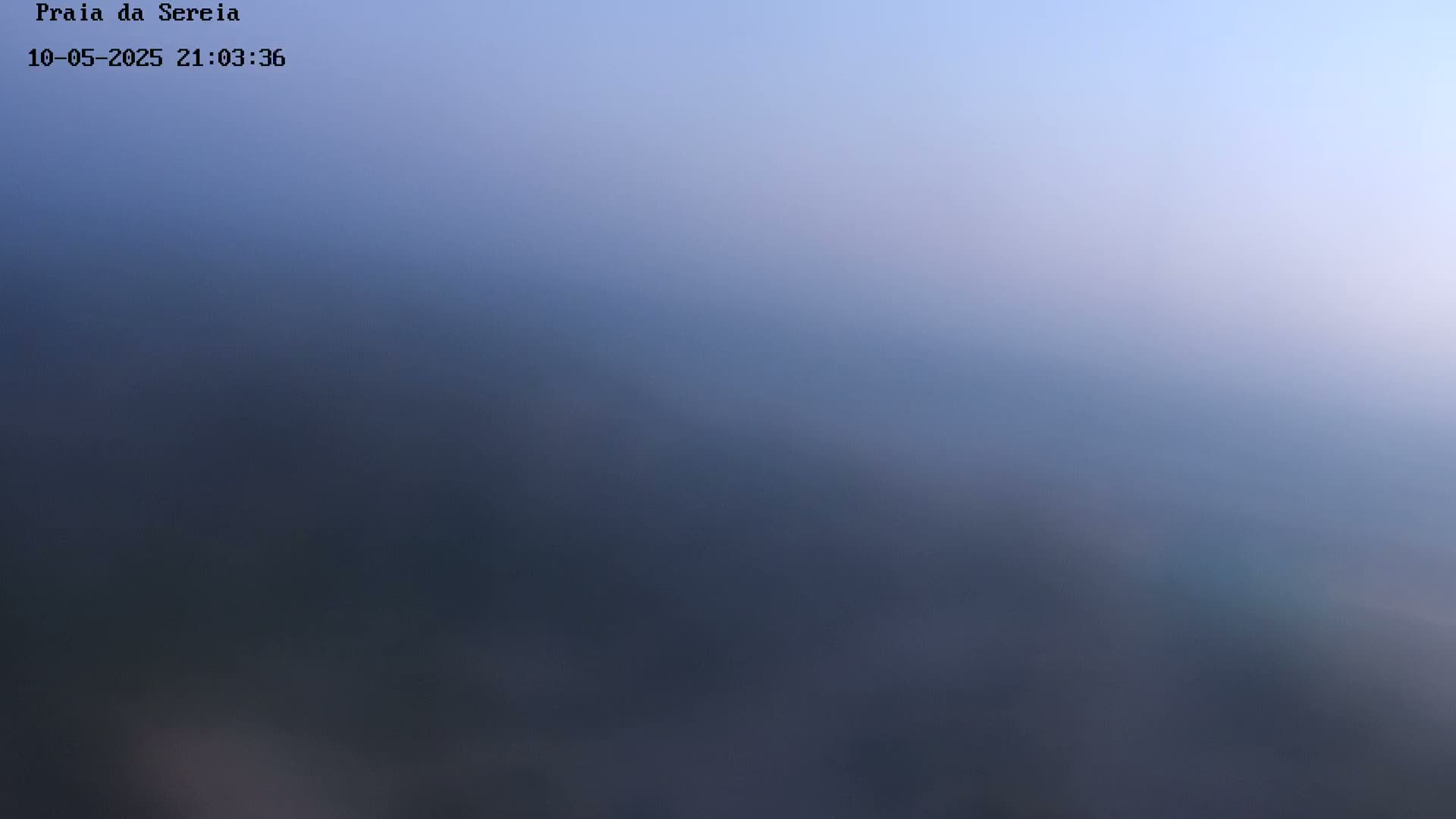 A blurry, out-of-focus image shows a hazy, dark blue landscape under a light blue sky at dusk or dawn.