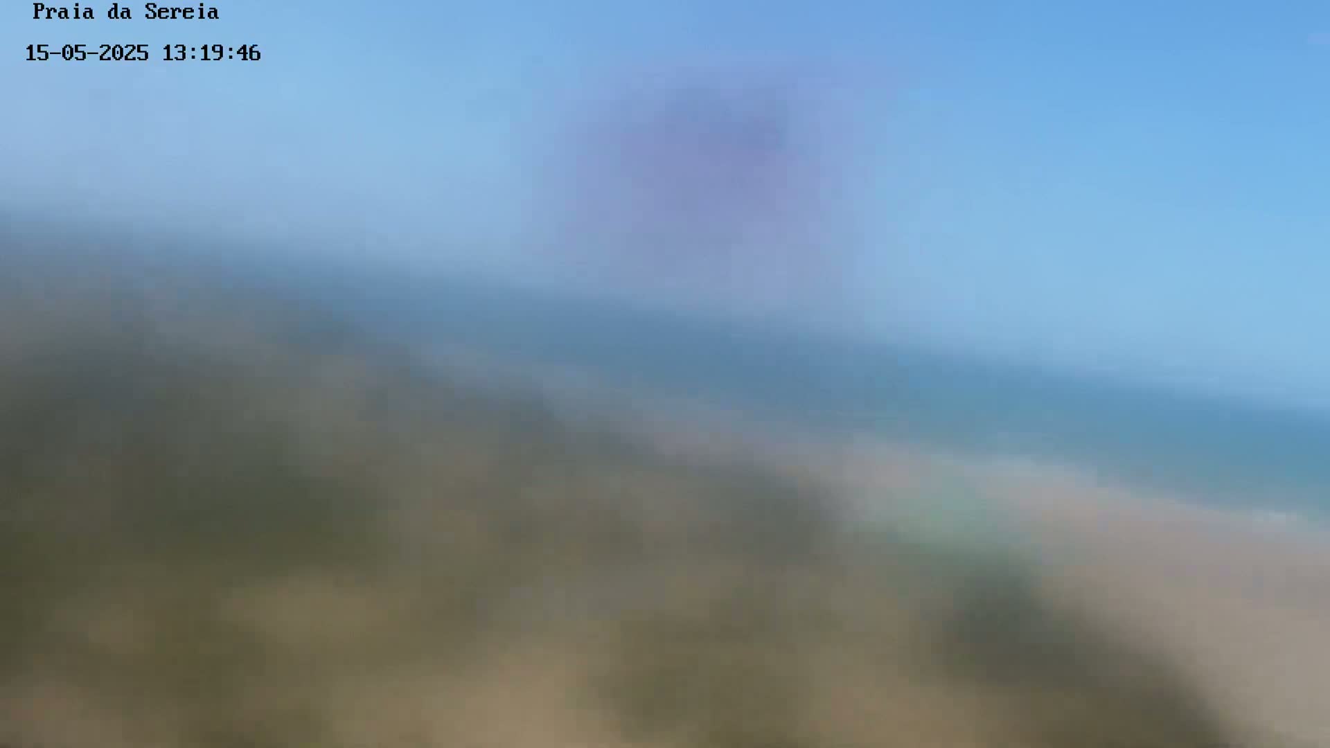 A blurry image shows a hazy, light-blue sky over a muted, indistinct beach scene.
