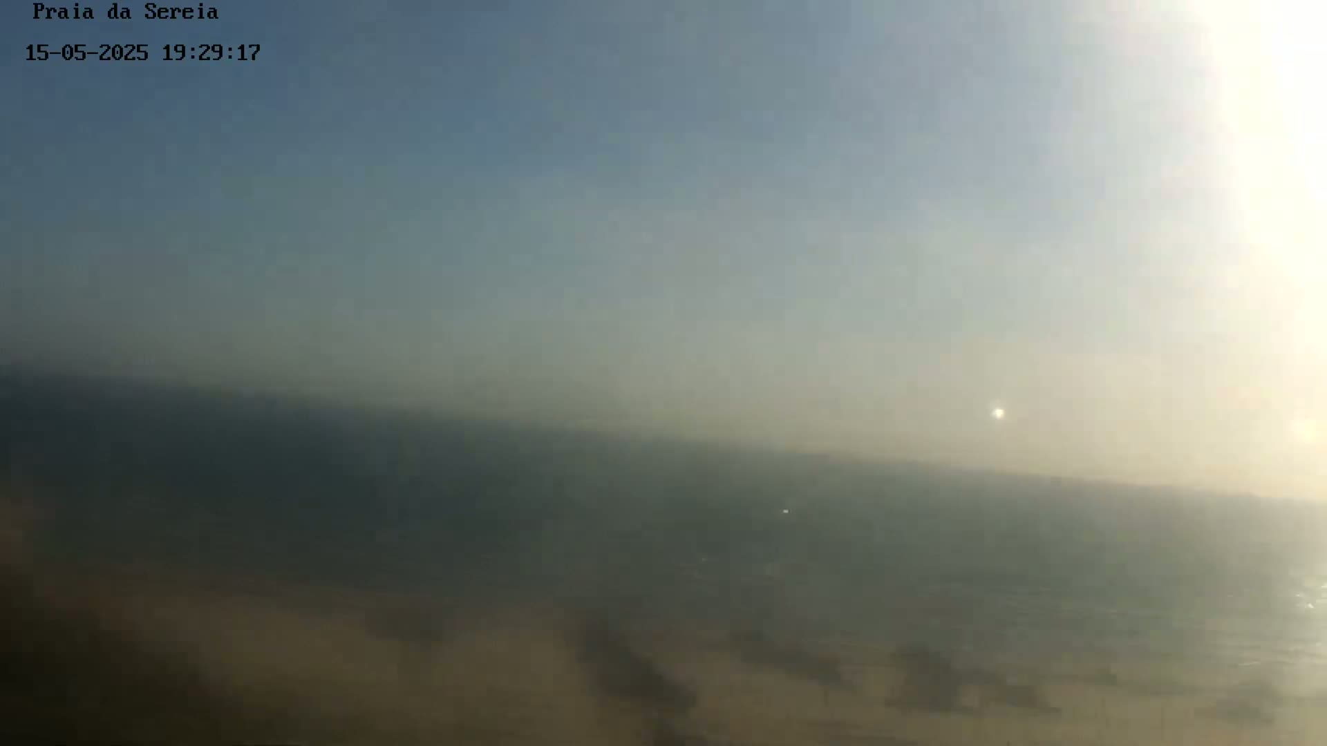 A hazy, sunlit view shows a beach and calm ocean under a mostly clear sky.