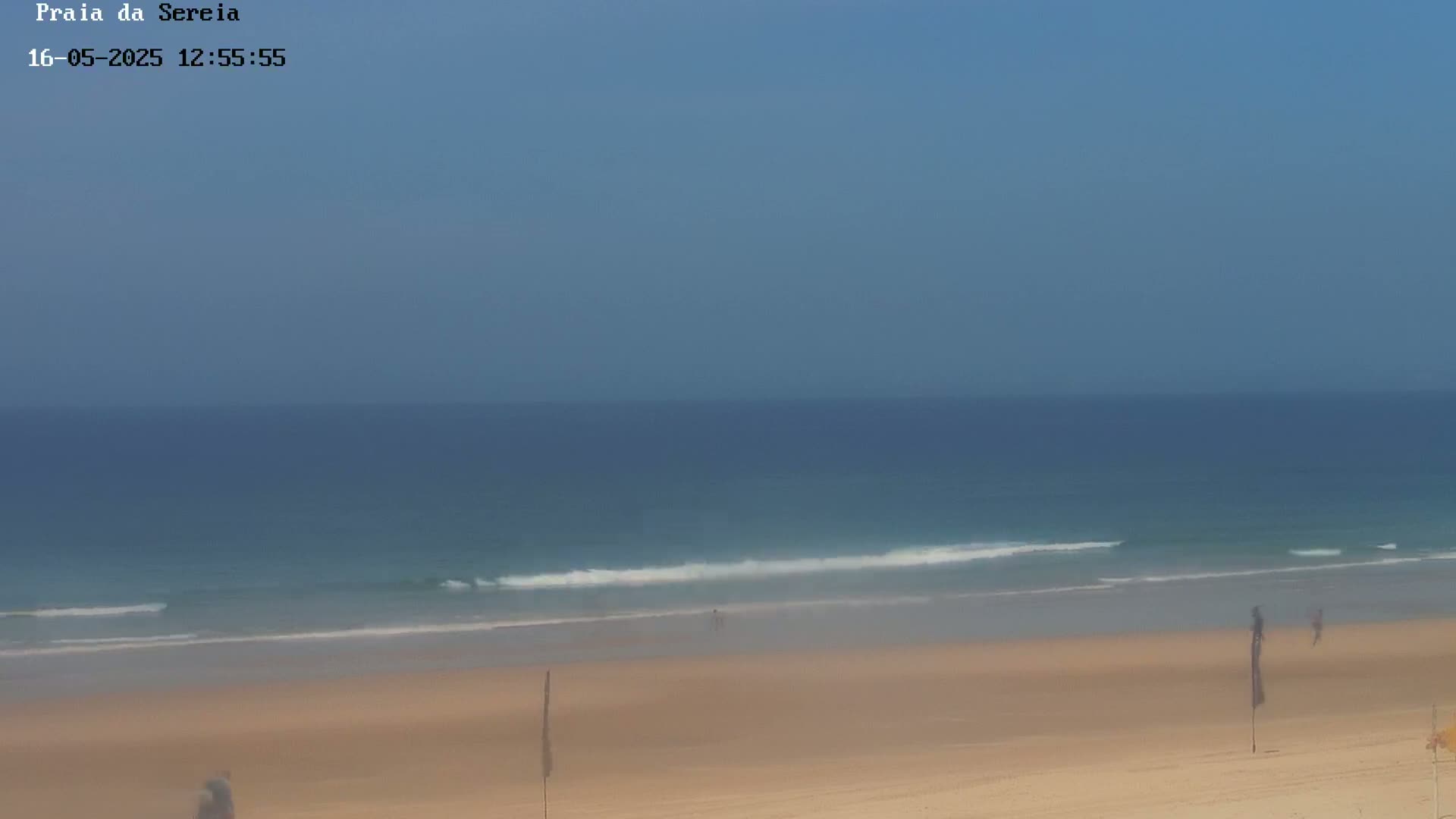 A sandy beach with calm ocean waves under a clear blue sky.