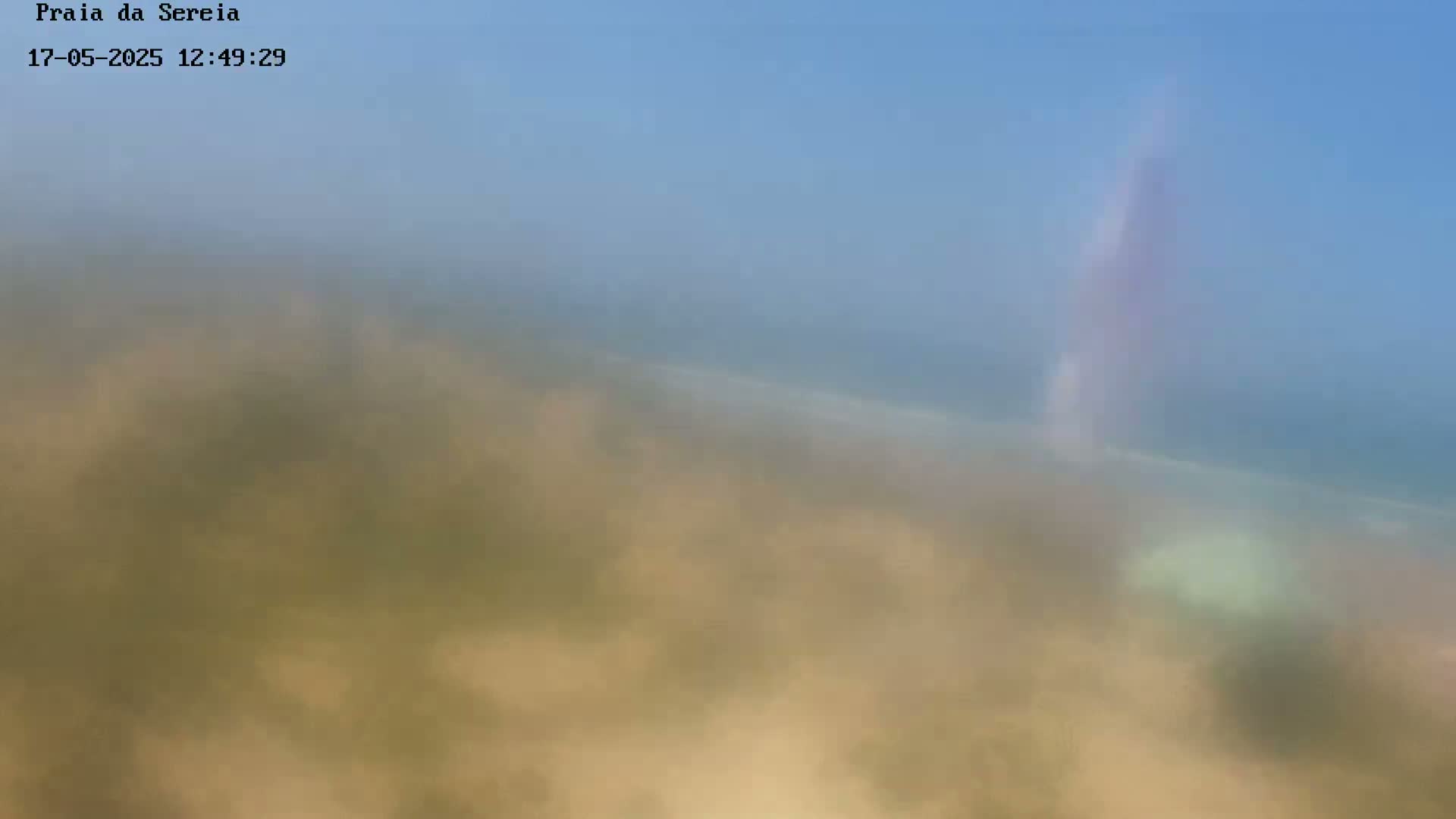 A hazy, out-of-focus image shows a light-brown sandy expanse leading to a blurry ocean under a clear blue sky.