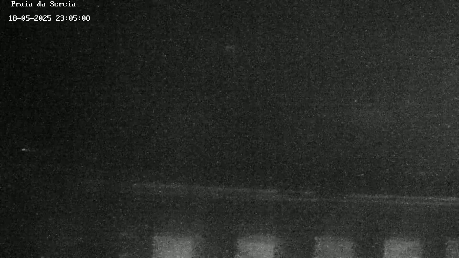 A dark, grainy nighttime image shows a mostly obscured, possibly beachside, scene with a faint horizontal line near the bottom.