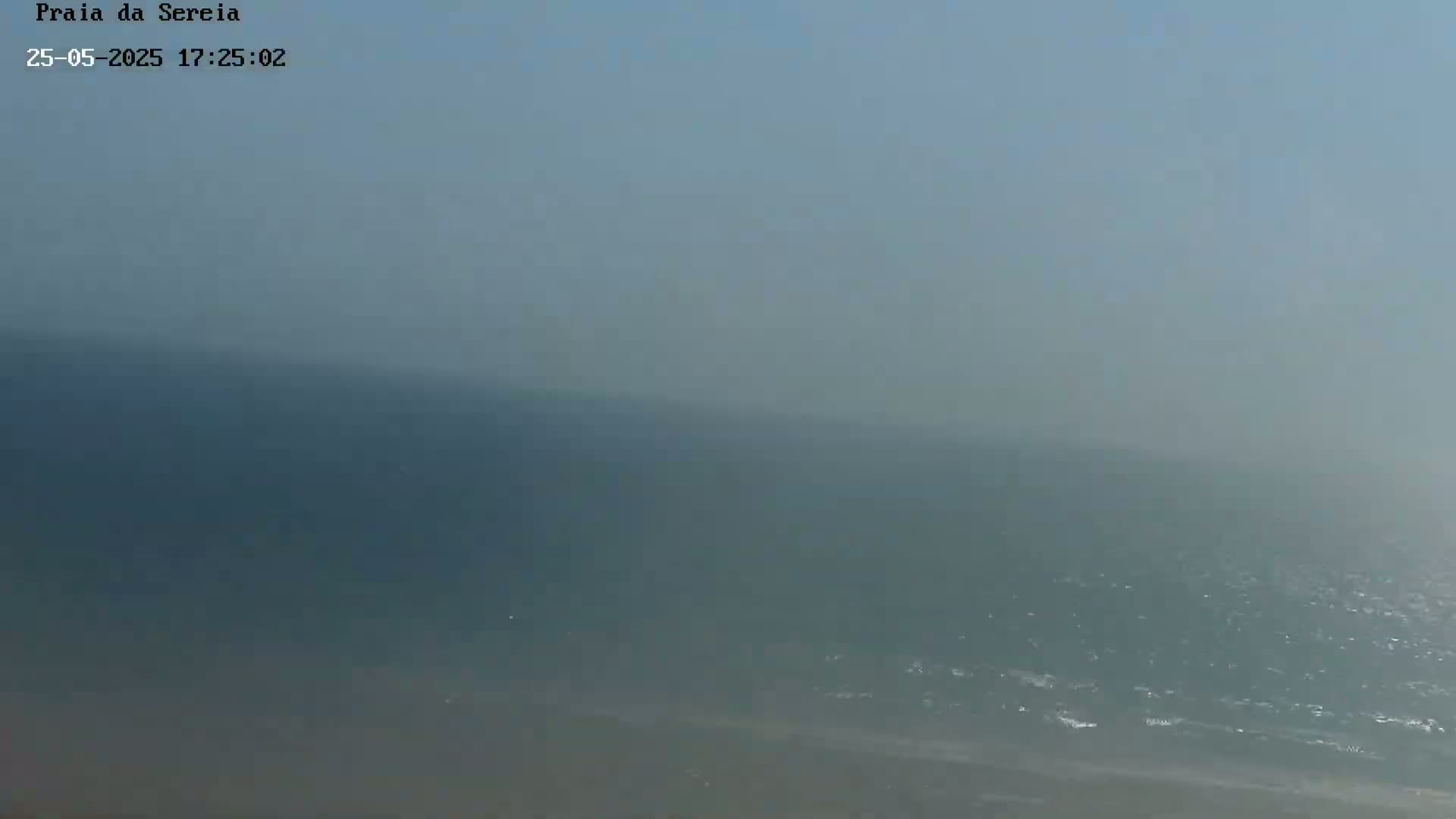 A hazy, somewhat overcast day shows a view of the ocean meeting a sandy beach.