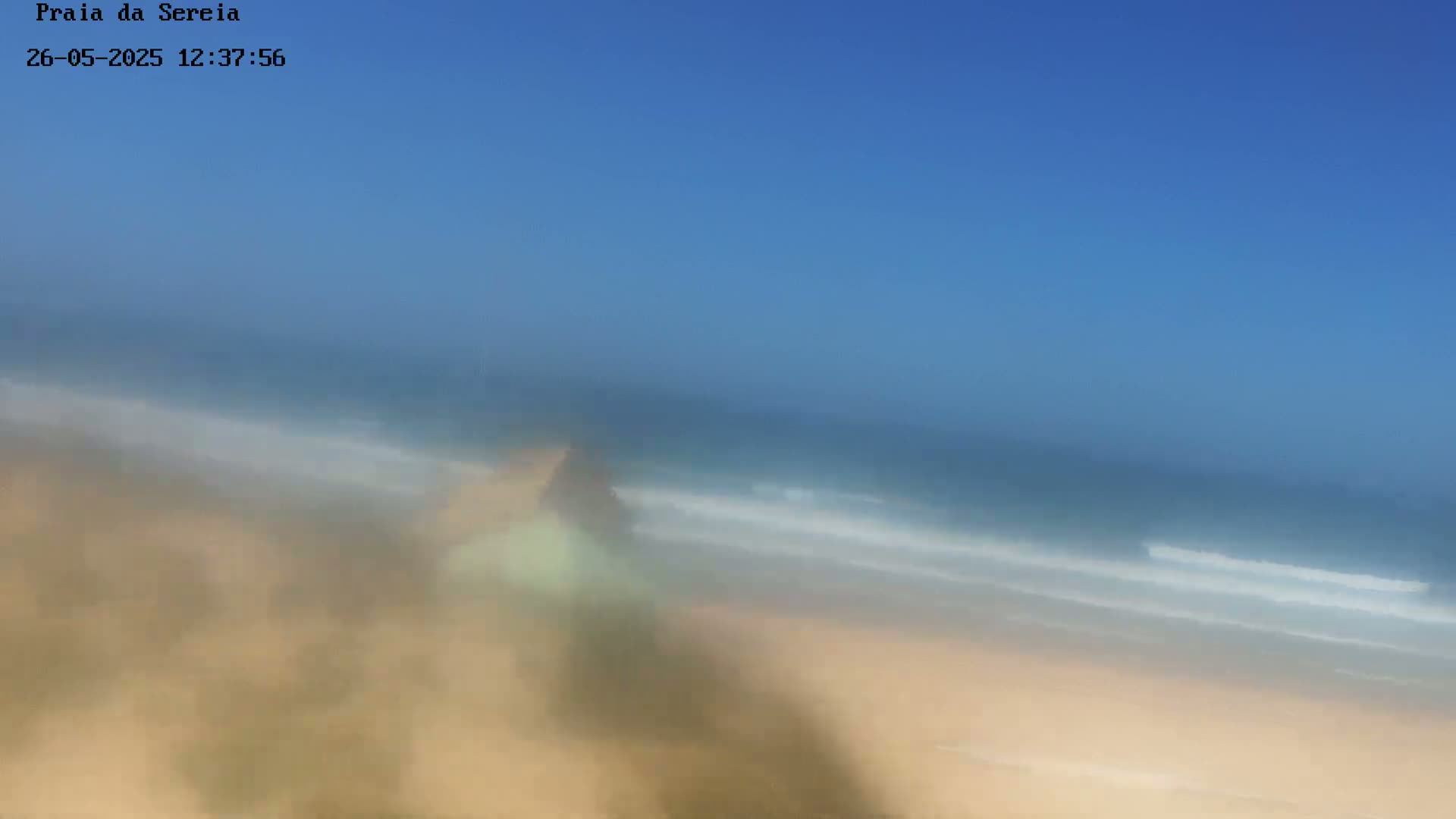 A hazy, blurry image shows a sandy beach and ocean under a clear blue sky.