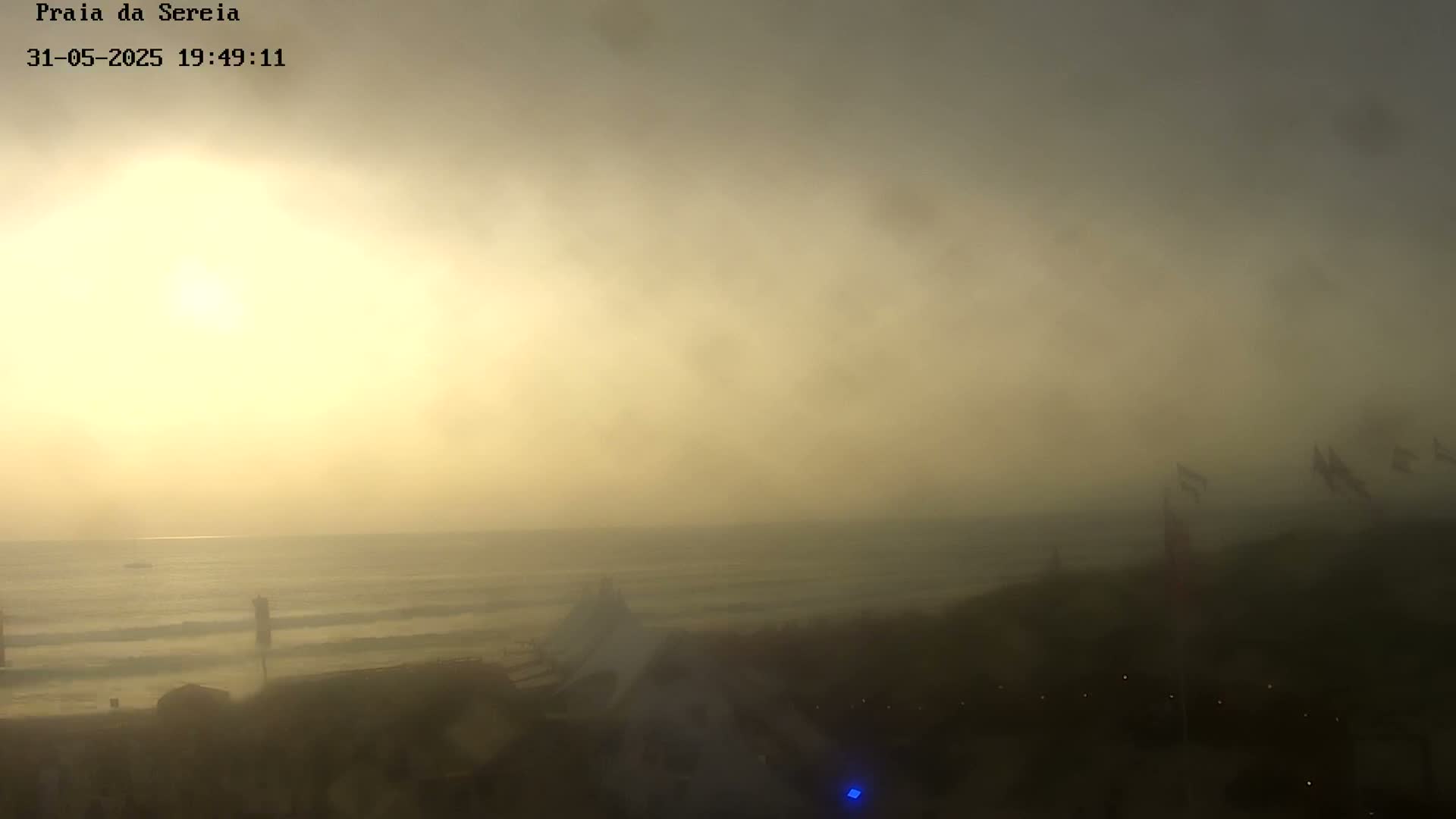 A hazy sunset over a beach with small waves, viewed from a high vantage point.