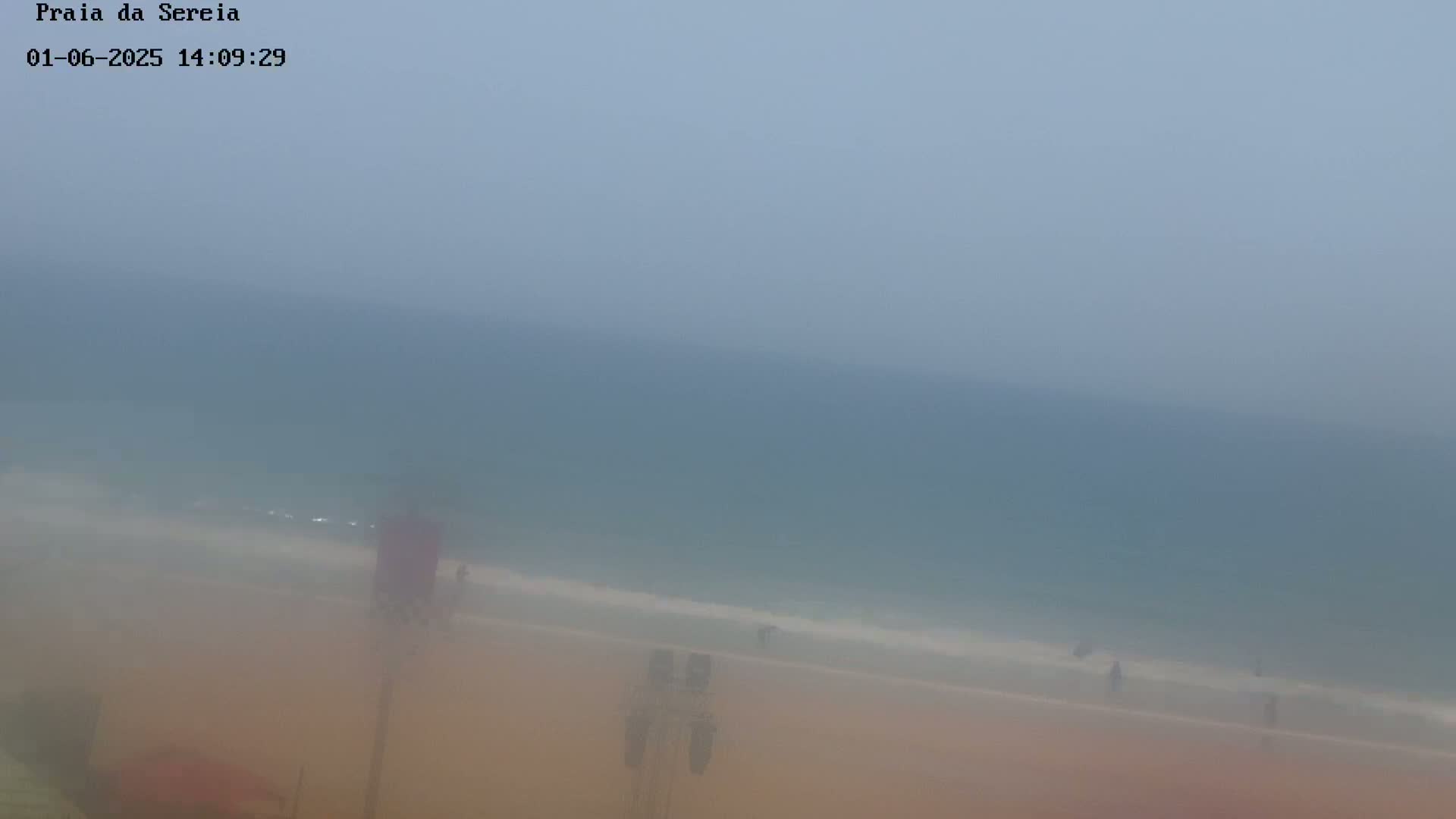 A hazy, overcast day at a beach shows a mostly empty sandy shore and calm, gray ocean in the distance.