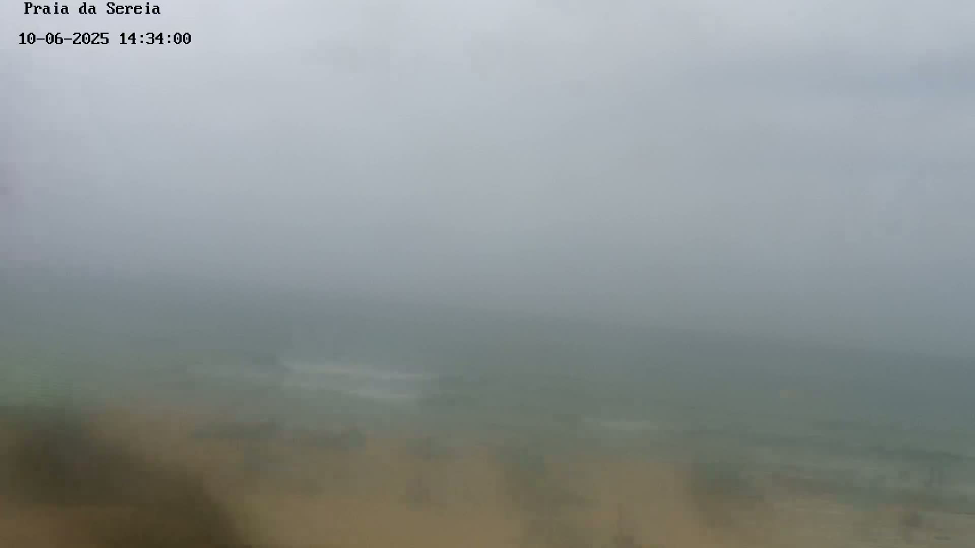 A foggy beach scene shows a muted expanse of sand and ocean, barely visible through a thick haze.