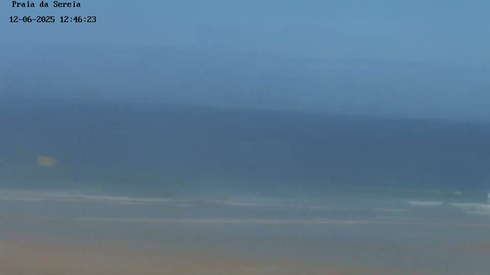 A hazy, overcast day shows a beach with calm waves gently rolling onto the shore.