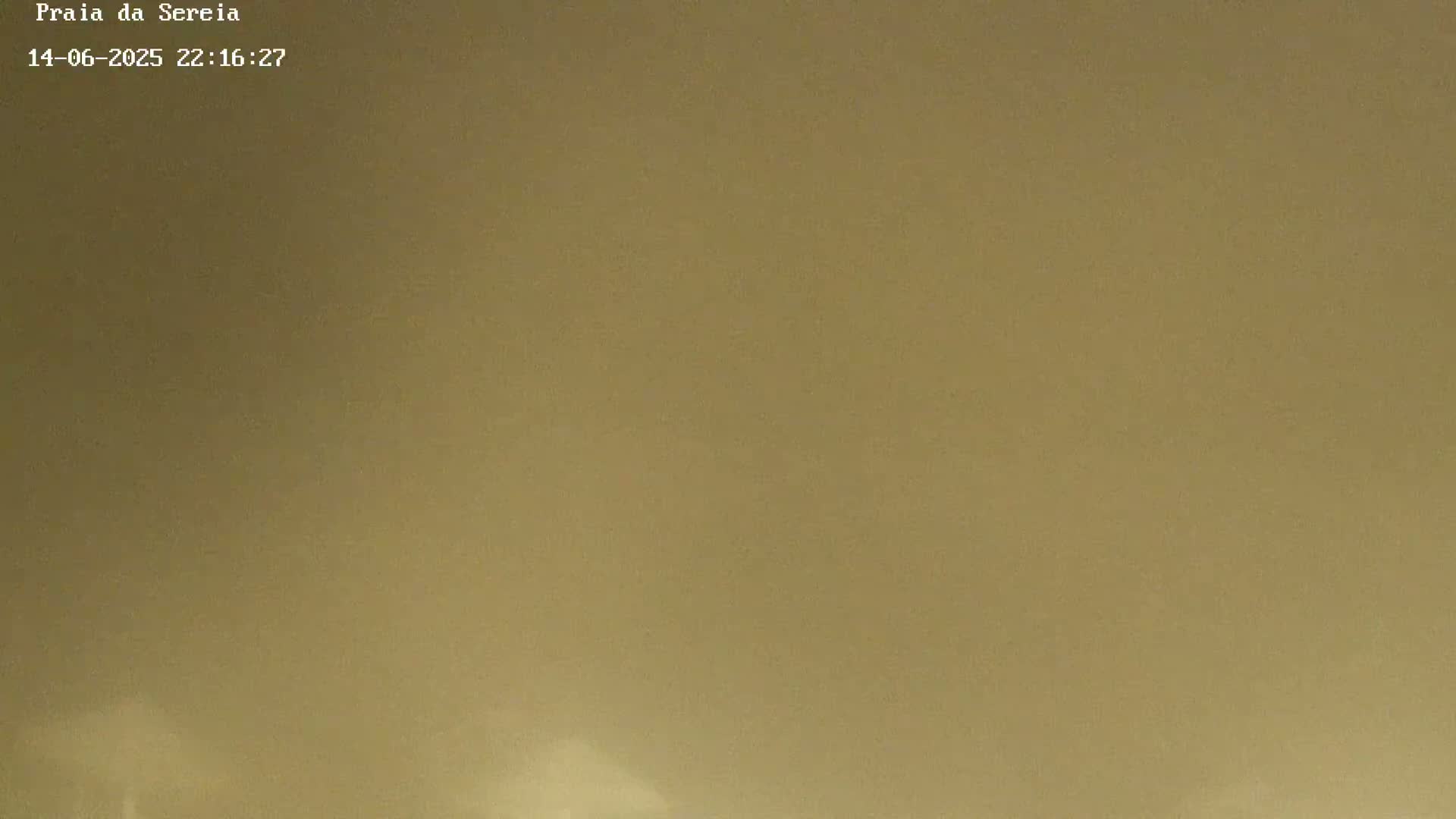 A hazy, misty view shows a beach with waves crashing on the shore under a mostly clear sky.