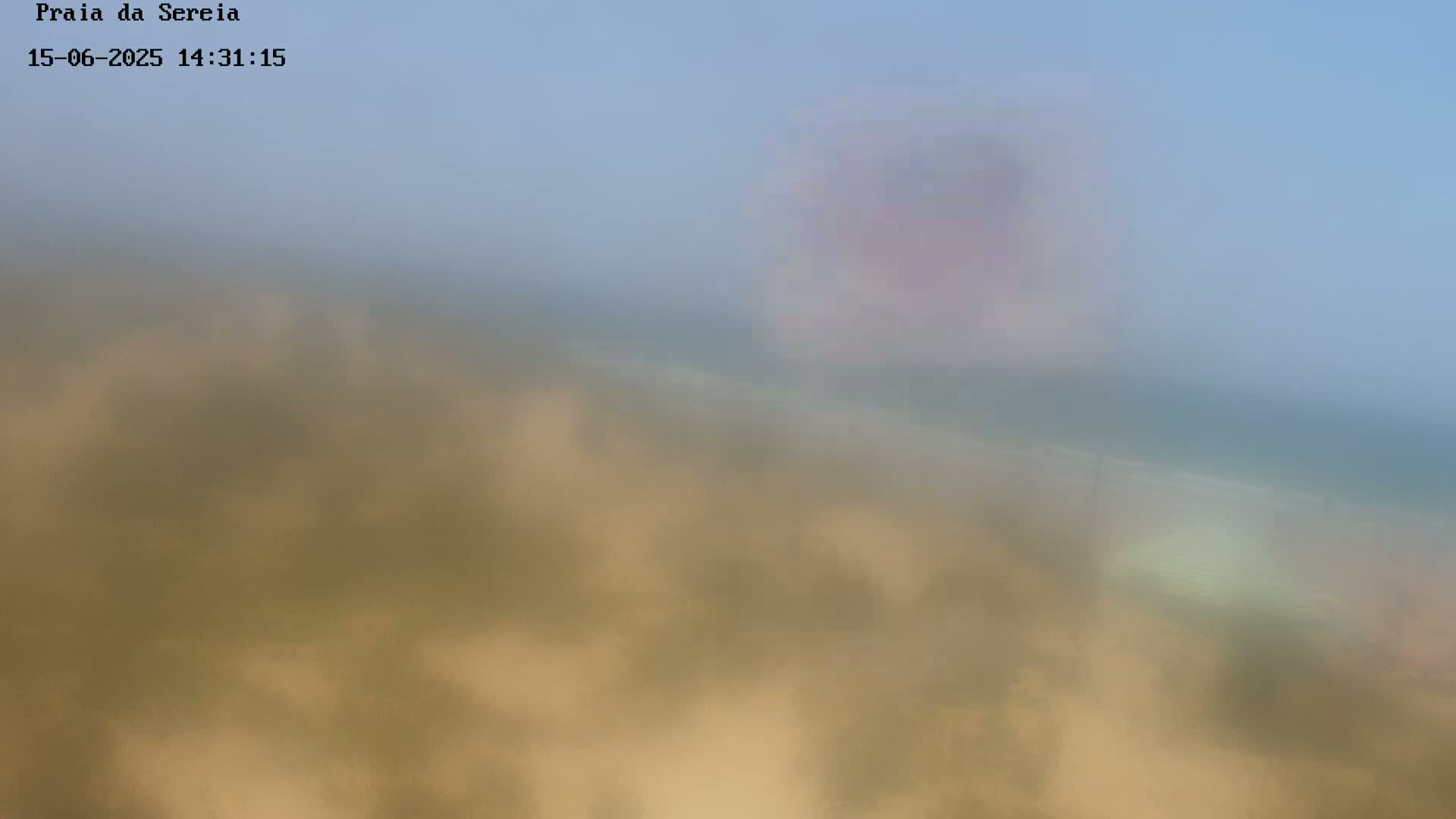 A hazy, blurry view of a sandy beach and ocean under a light blue sky.