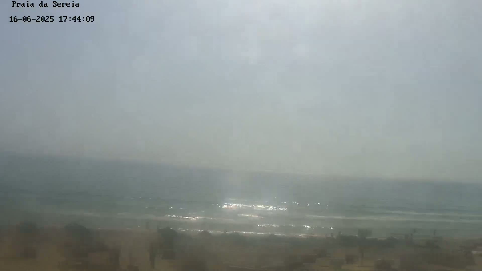 A hazy, overcast day shows a beach with gentle waves lapping the shore.