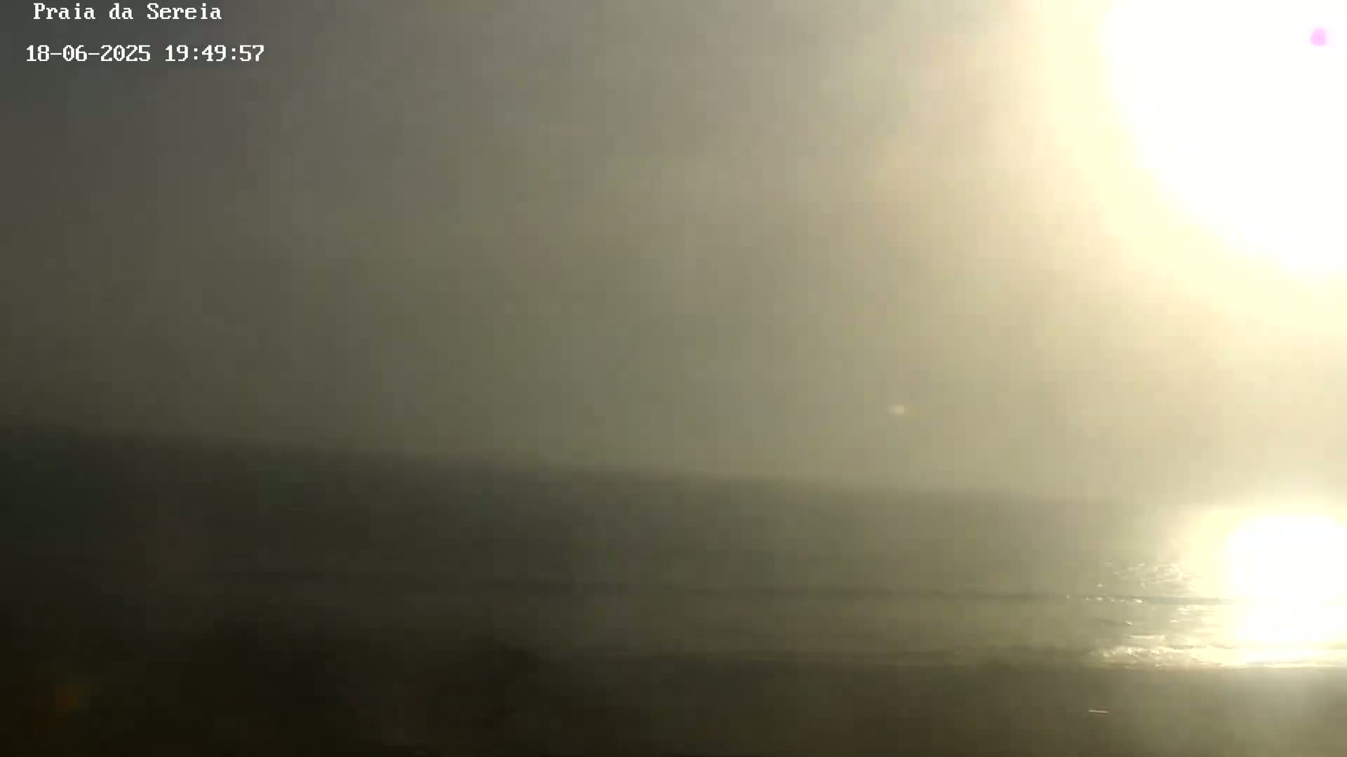 A hazy sunset over a calm ocean beach.