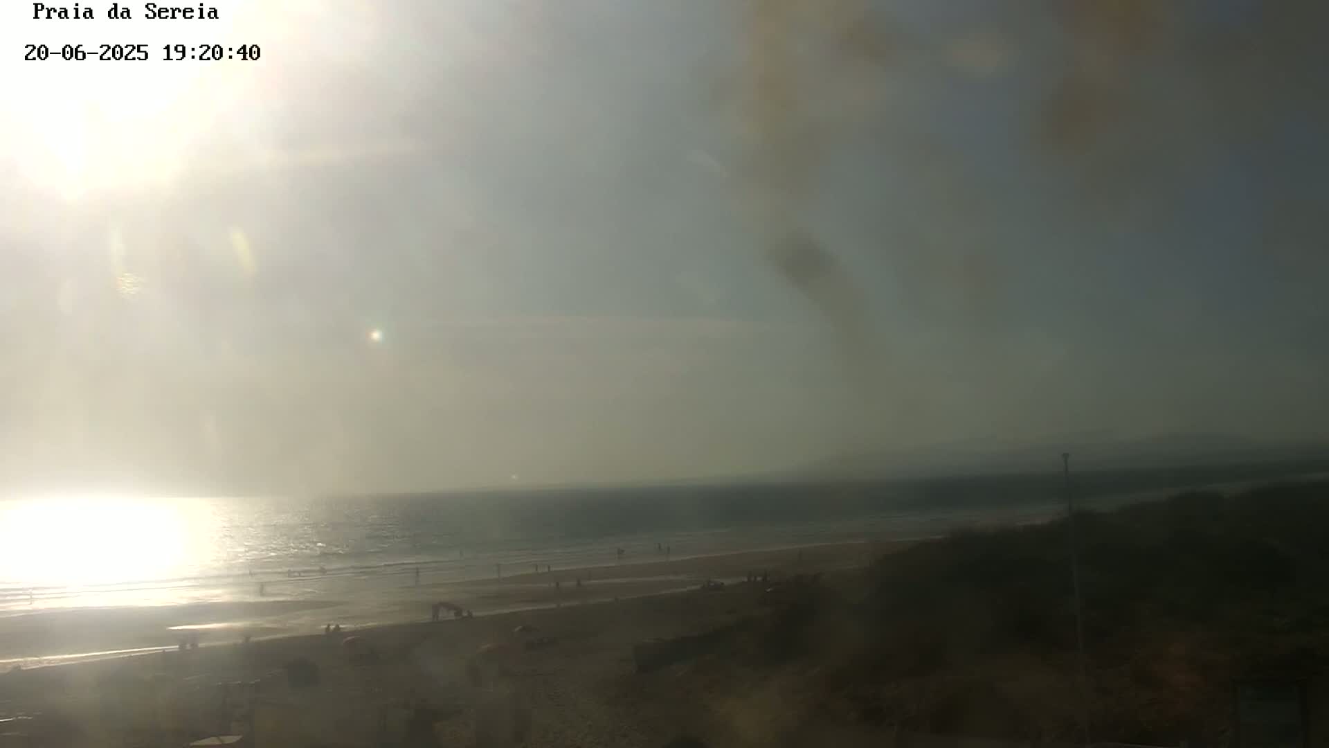 A hazy sunset over a beach with a few people visible on the sand and in the water.