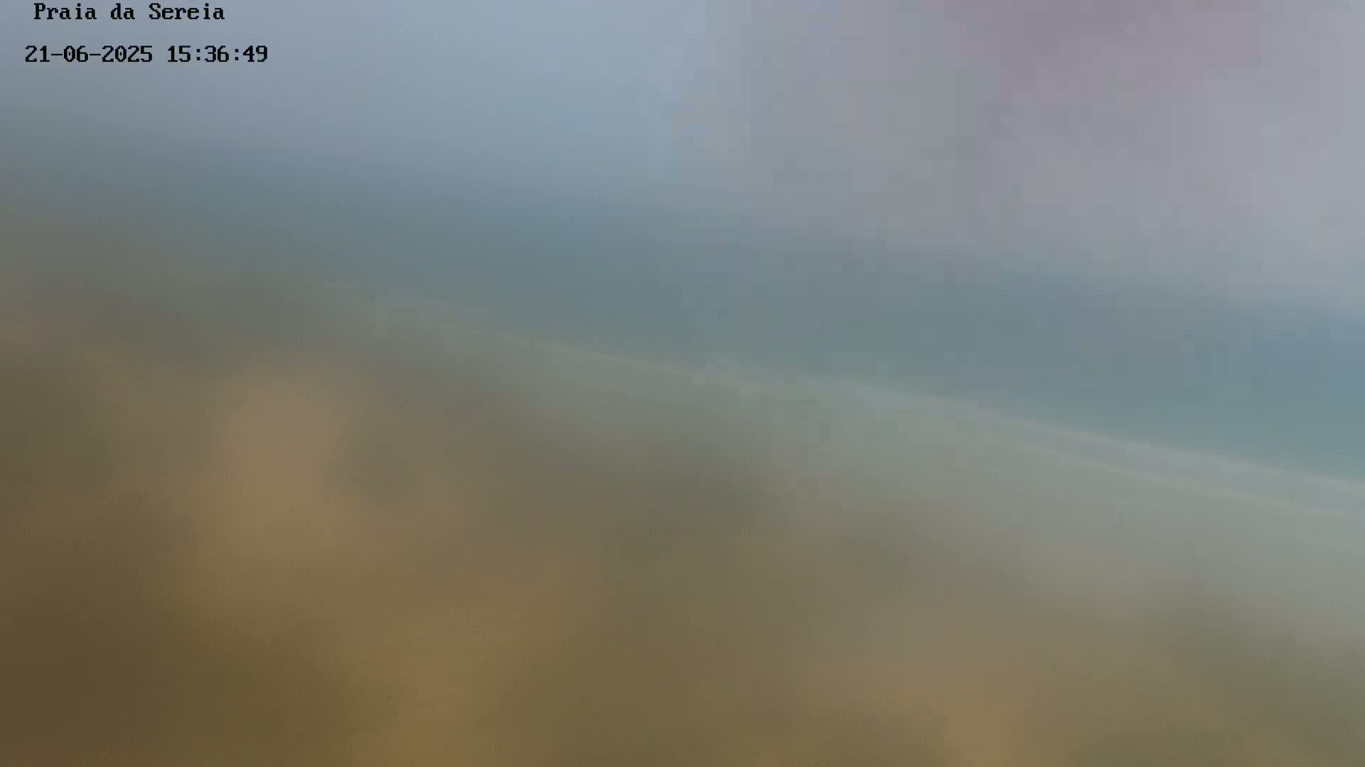 A hazy view of a beach and ocean is seen on an overcast day.