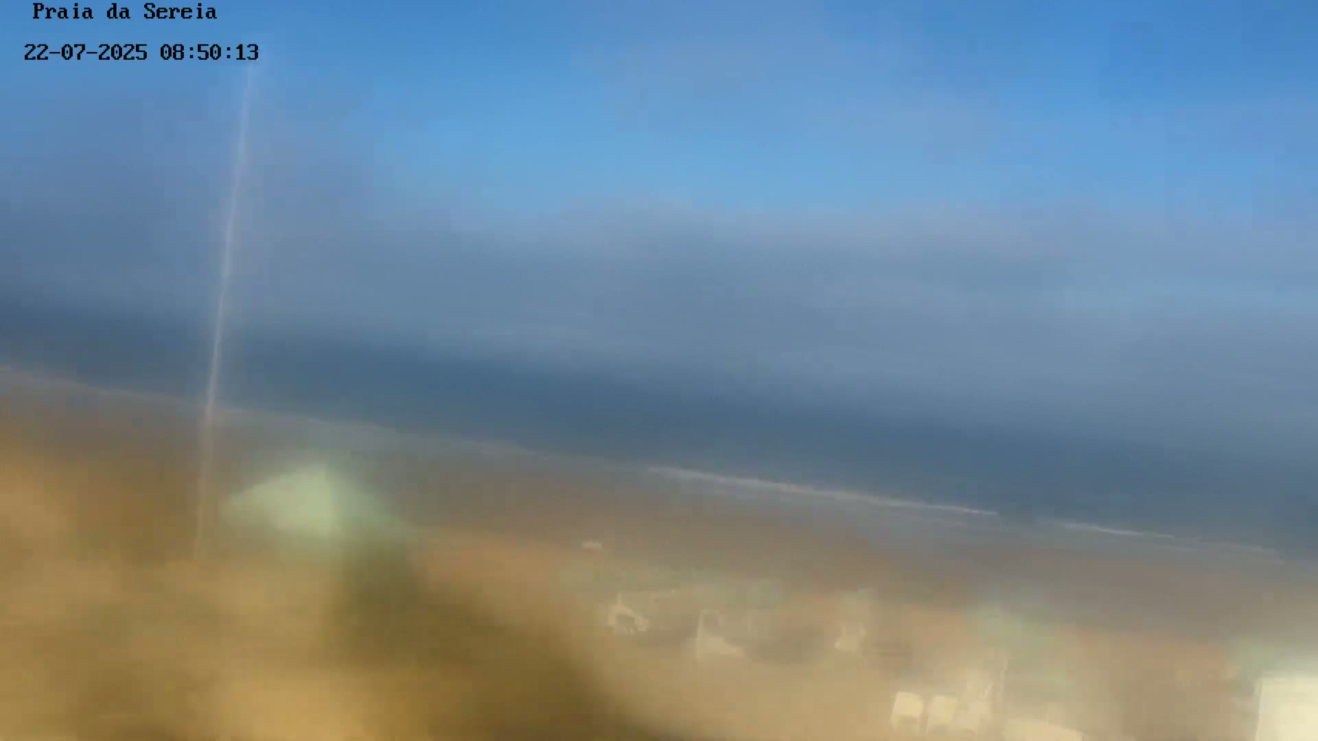 A hazy view shows a beach with a calm ocean under a clear blue sky.