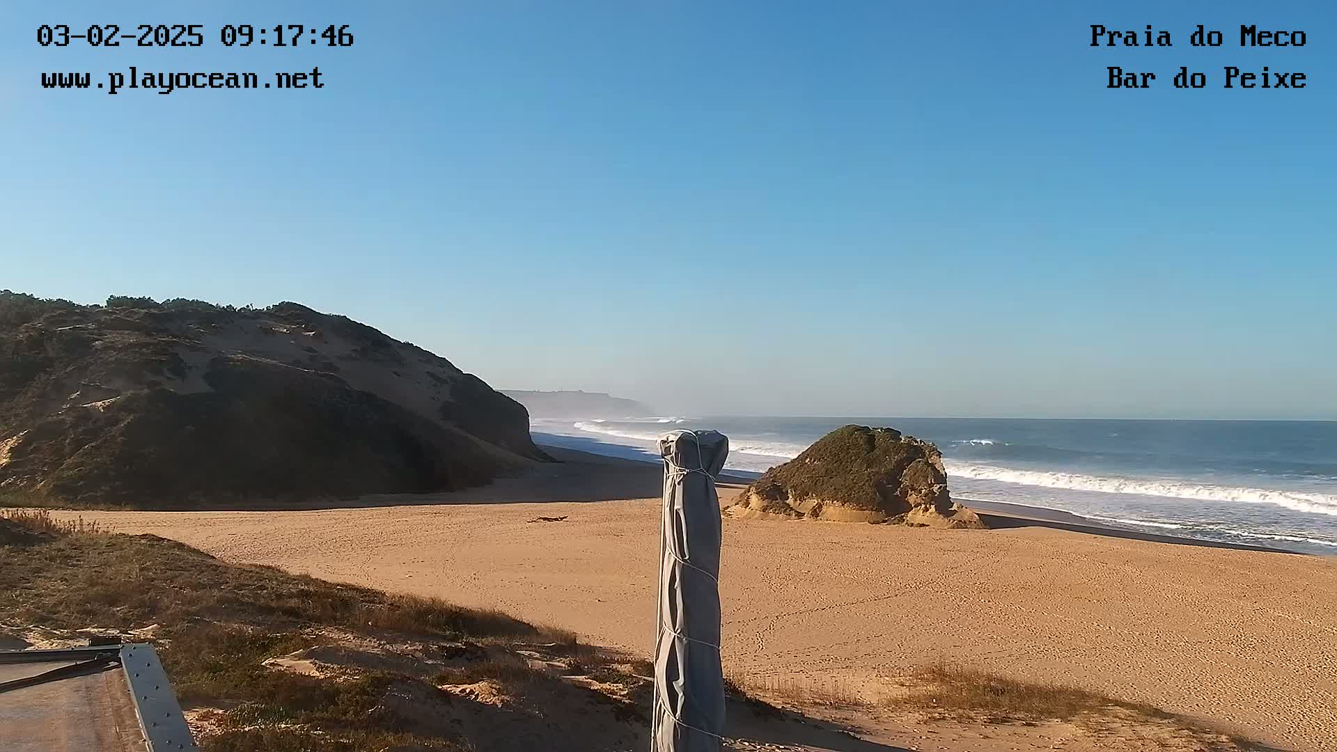 A sandy beach with small cliffs and rolling waves under a clear blue sky.