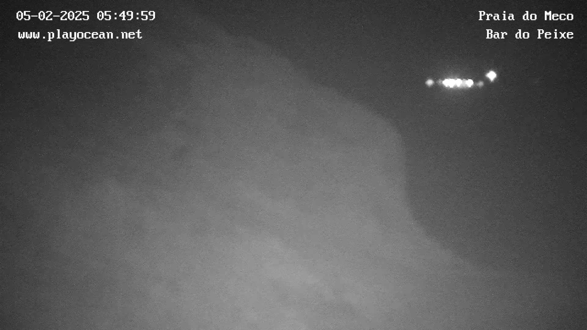 A grainy, dark nighttime image shows a blurry, indistinct shoreline with a few distant lights visible in the dark.