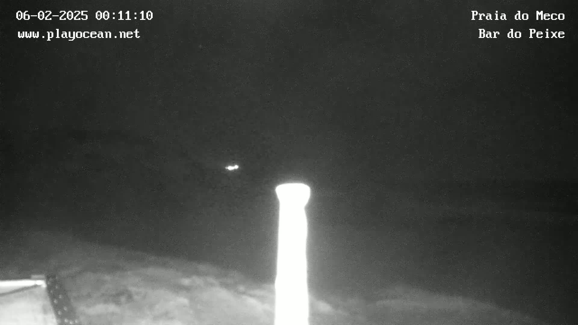 A tall, bright, vertical structure is visible against a dark, nighttime sky with faint clouds.