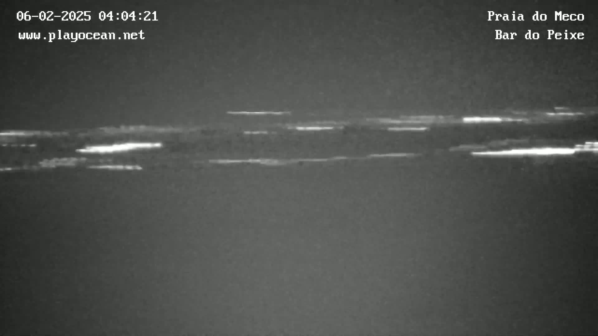A nighttime, low-light image shows a dark body of water with faint, horizontal white streaks of light on its surface.